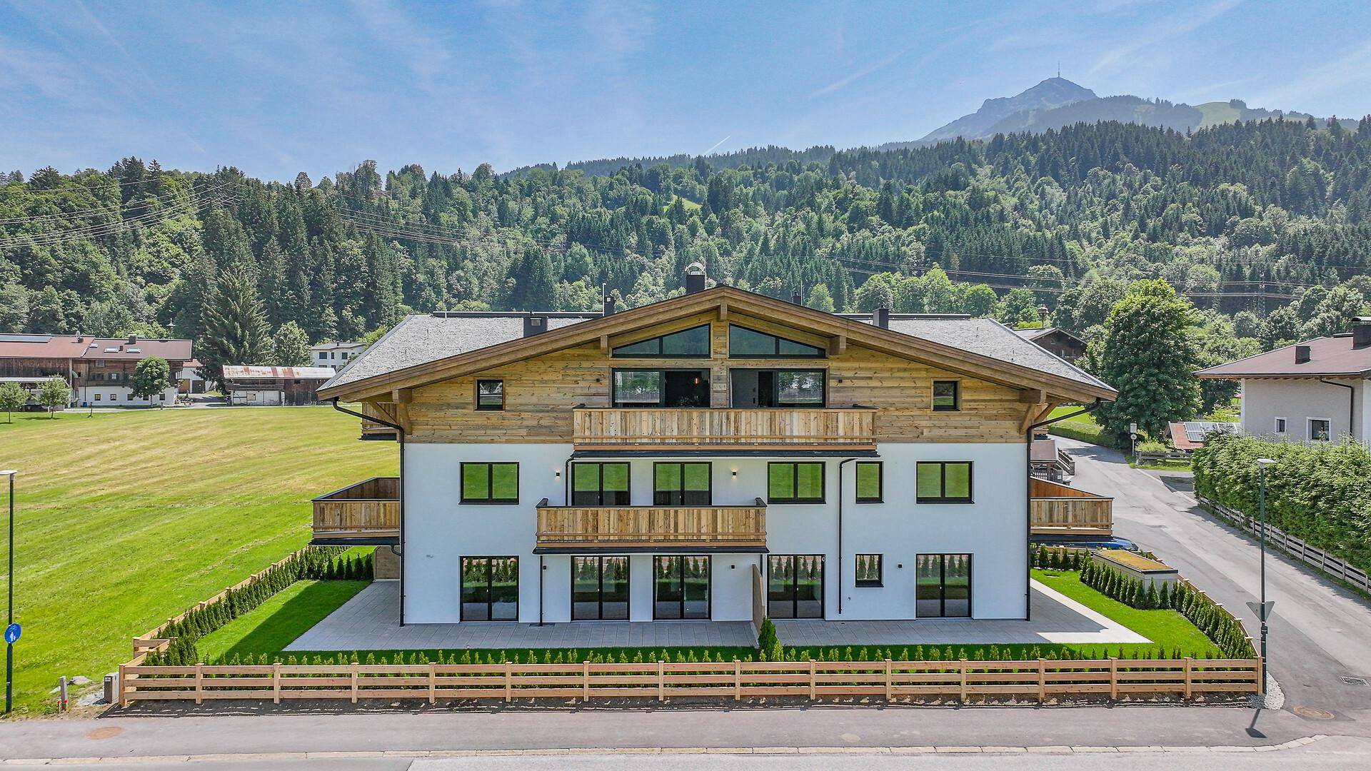 Modernes Wohngebäude im alpinen Stil mit Holzelementen und Balkonen, umgeben von Natur.