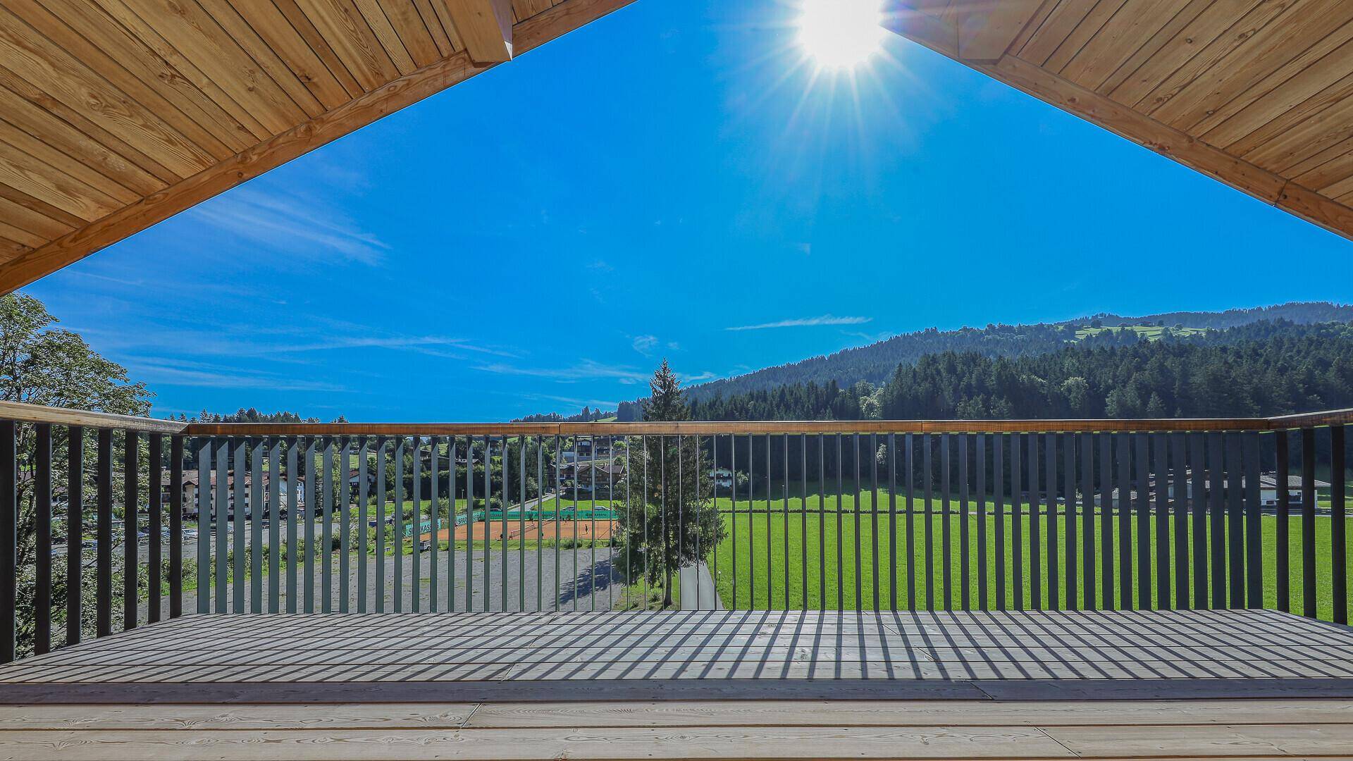 Großer Holzbalkon mit weitem Blick auf die grüne Landschaft und die Berge unter blauem Himmel.