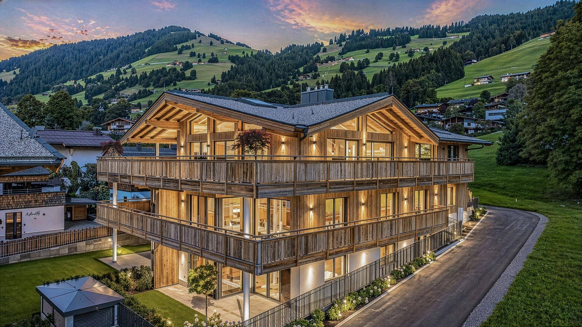 Attraktives Mehrfamilienhaus in alpiner Architektur bei Sonnenuntergang mit beleuchteten Balkonen.