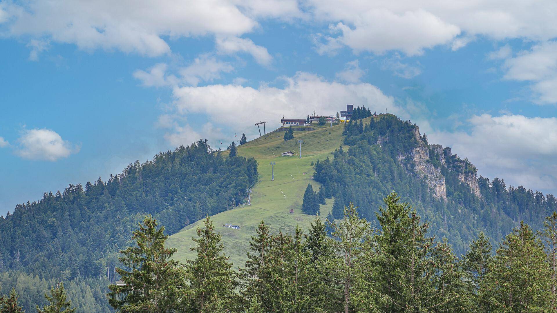 Berglandschaft mit Skipiste, Liftanlagen und bewaldeten Hängen unter blauem Himmel.
