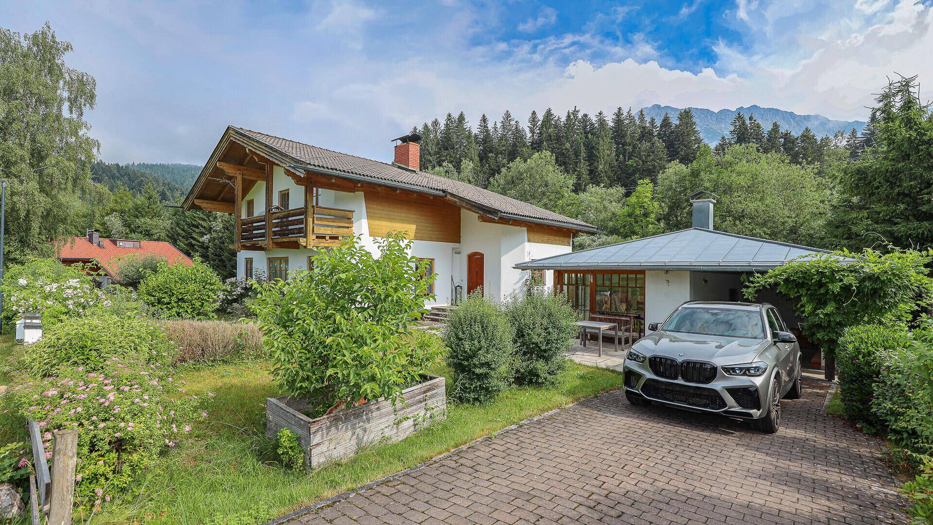 Haus im alpenländischen Stil mit gepflasterter Auffahrt und einem modernen SUV davor.