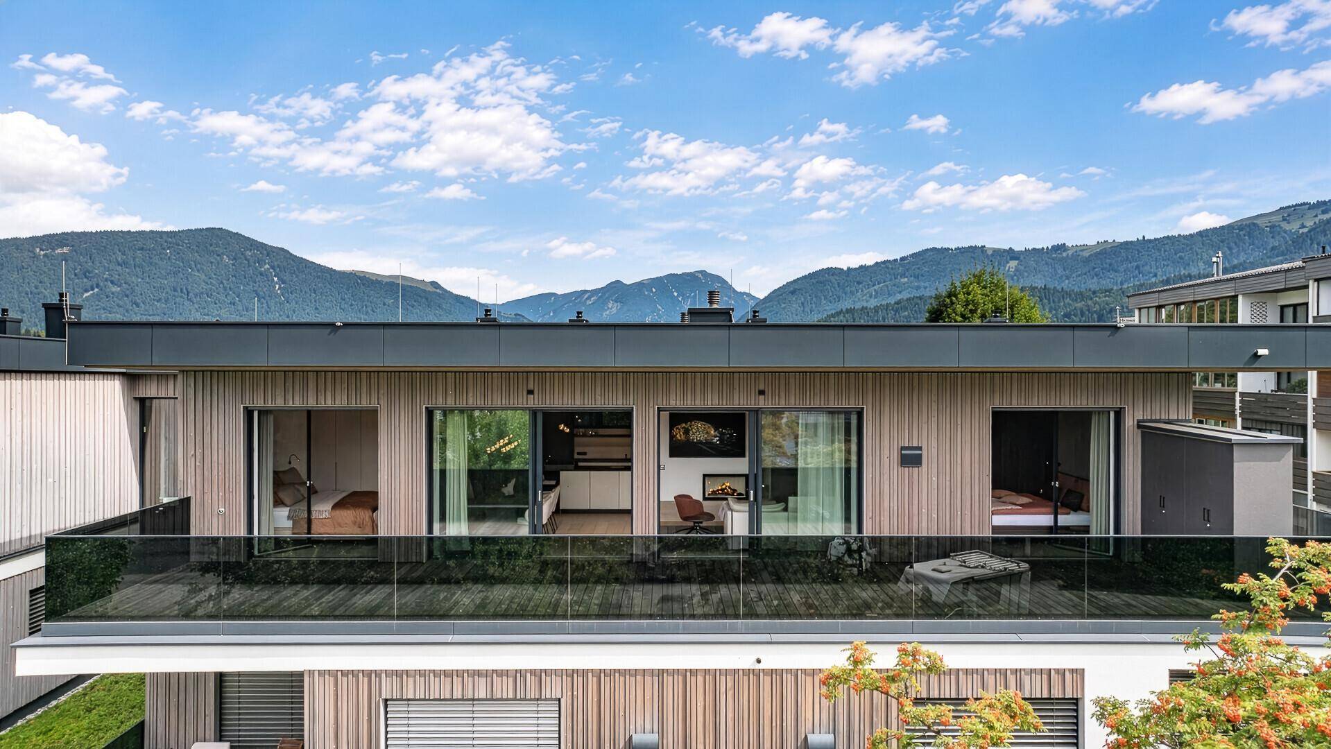Moderne Gebäudefassade mit Holzverkleidung, großen Fensterfronten und Bergblick.