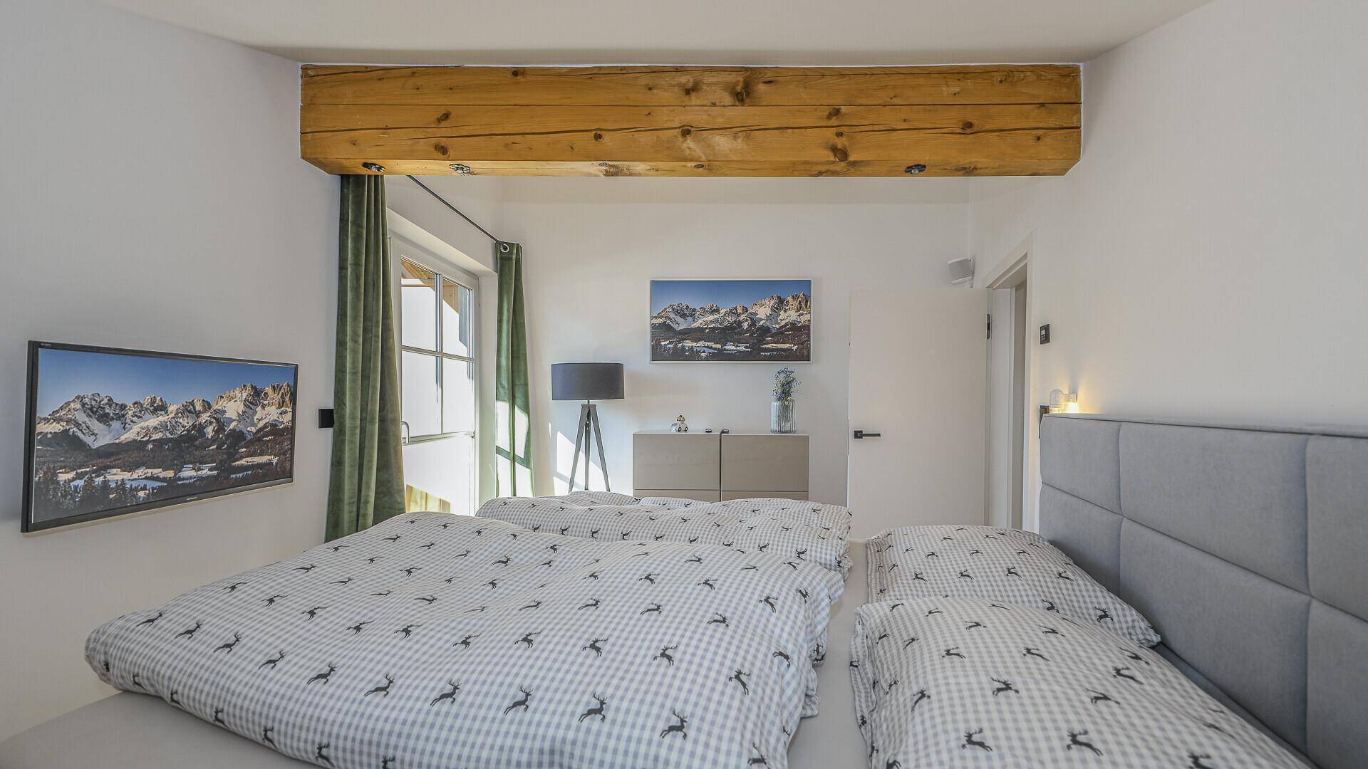 Helles Schlafzimmer mit Doppelbett, sichtbarem Holzbalken und Fenster mit Blick ins Grüne.