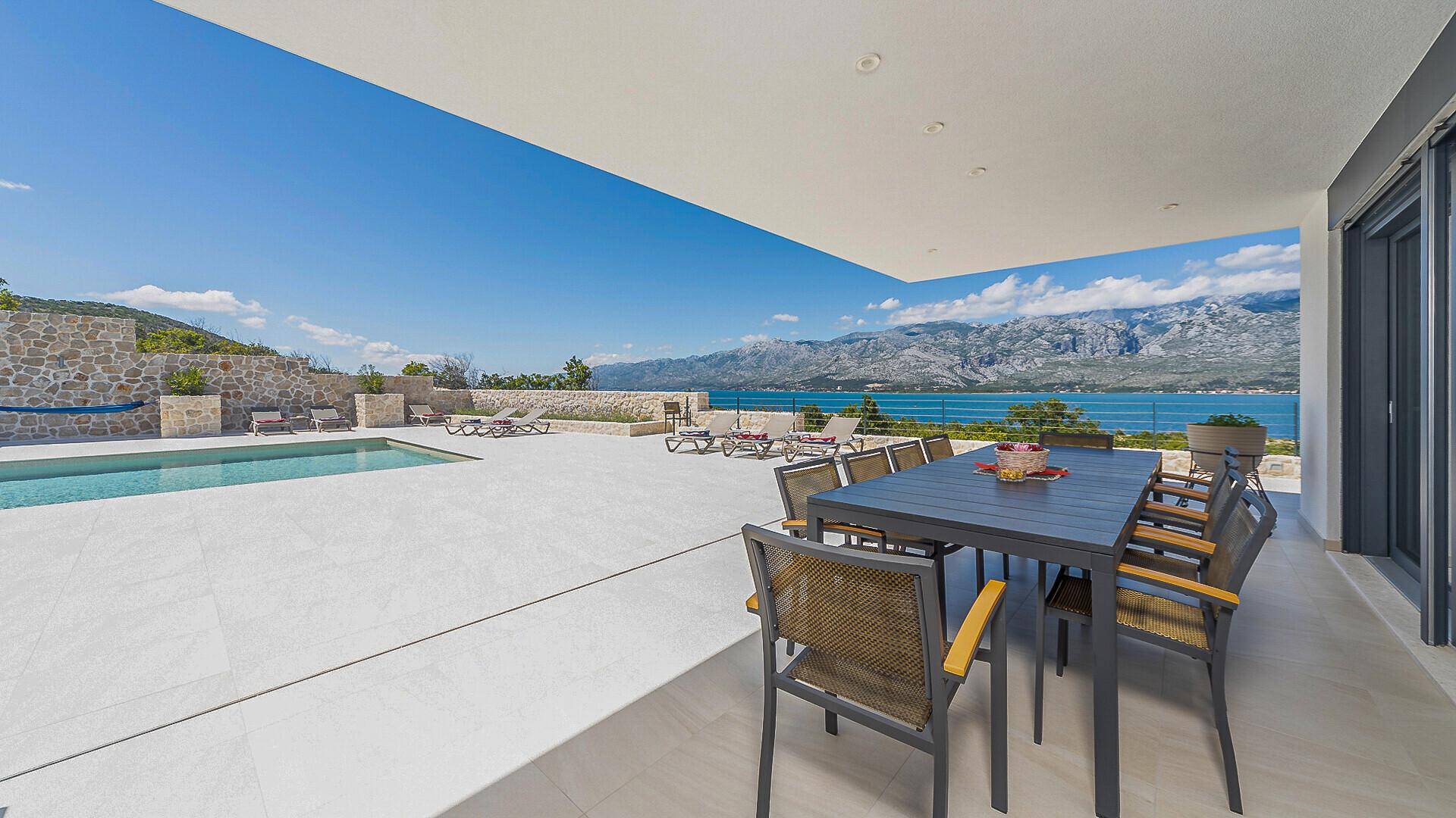 Überdachte Terrasse im Erdgeschoss mit Esstisch und direktem Blick auf den Poolbereich und das Meer.