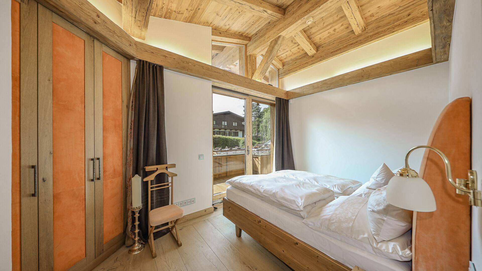 Schlafzimmer mit integrierten Kleiderschränken, Holzbalkendecke und Balkonzugang.