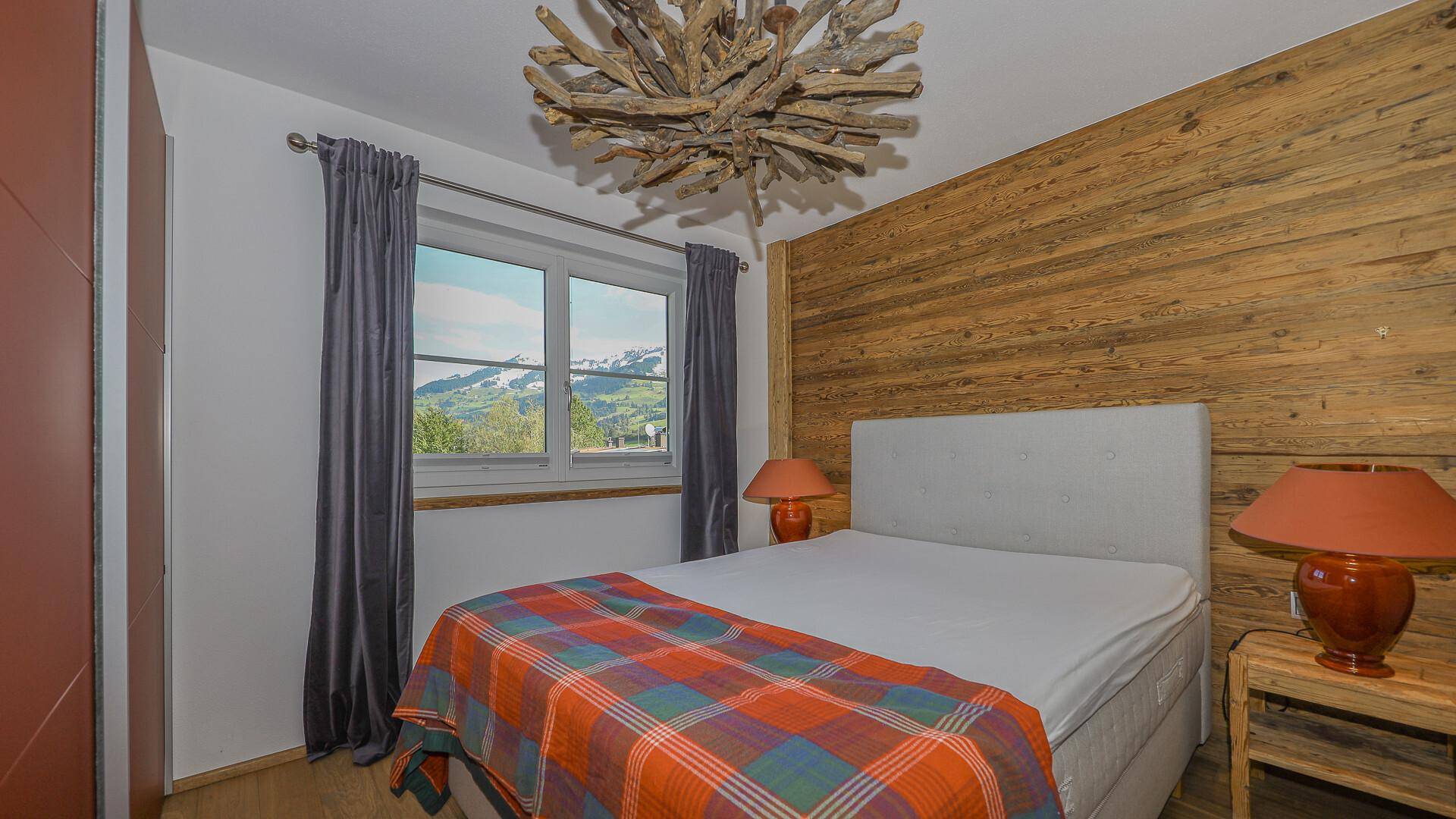 Schlafzimmer mit Holzwand, Doppelbett und Fenster mit weitem Blick auf die Berge.