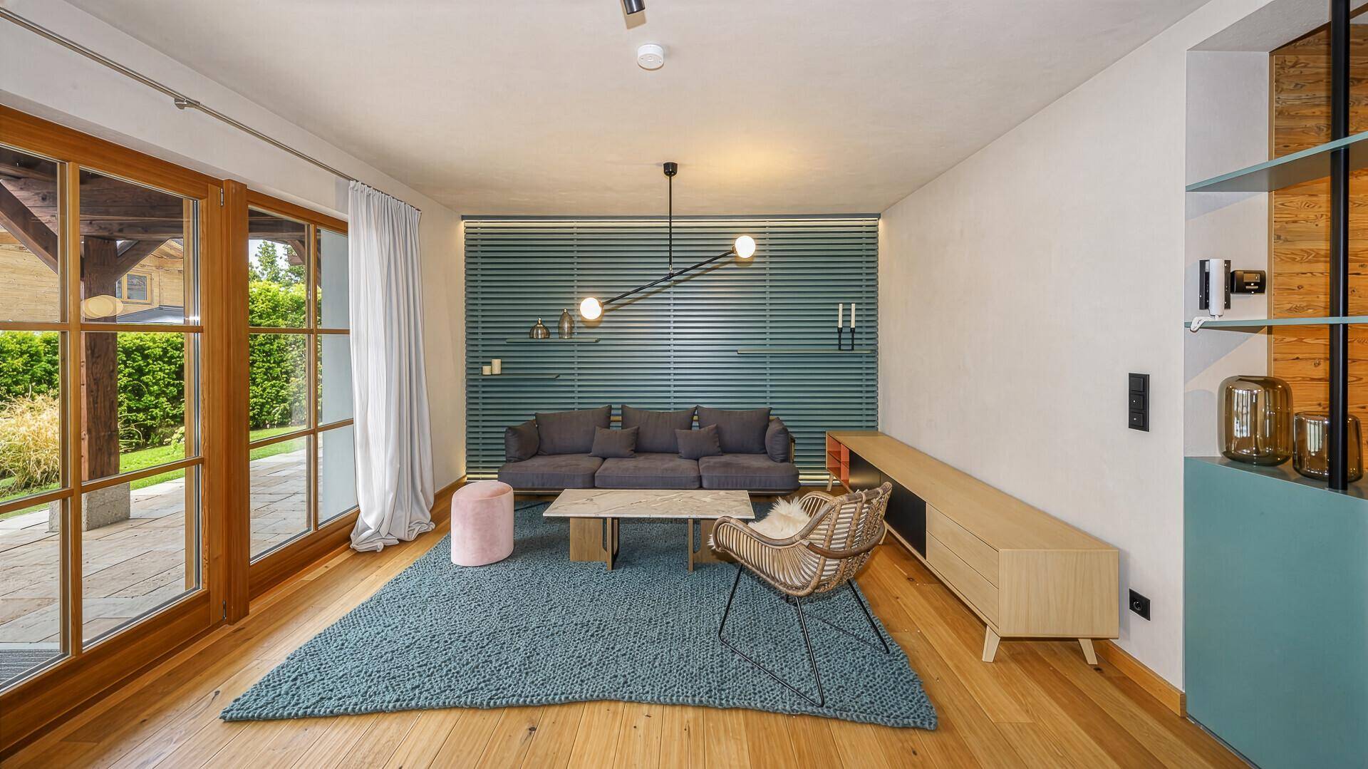Modern eingerichtetes Wohnzimmer mit Holzboden und Zugang zum Außenbereich durch große Fenster.
