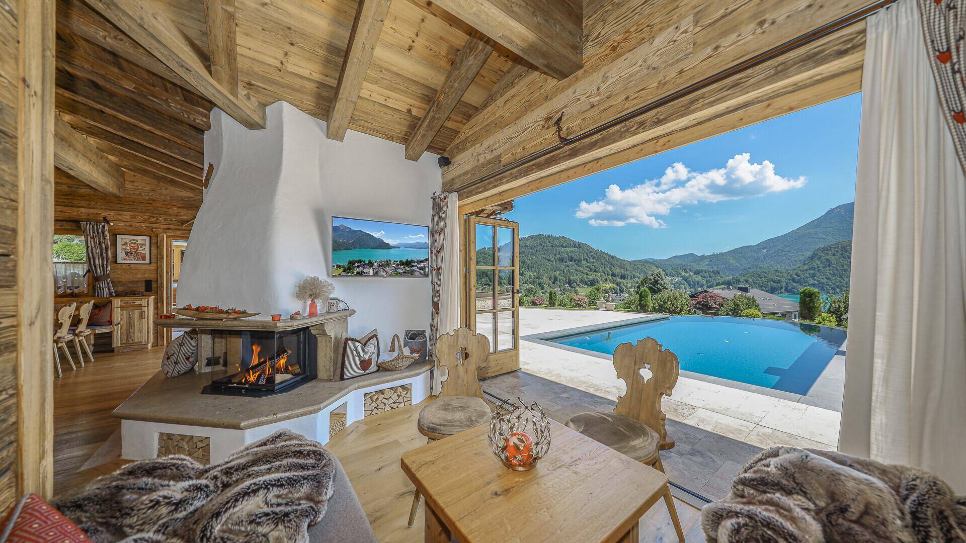 Gemütlicher Wohnbereich im Holzhaus mit Kamin, Holzbalken und direktem Zugang zum Pool.