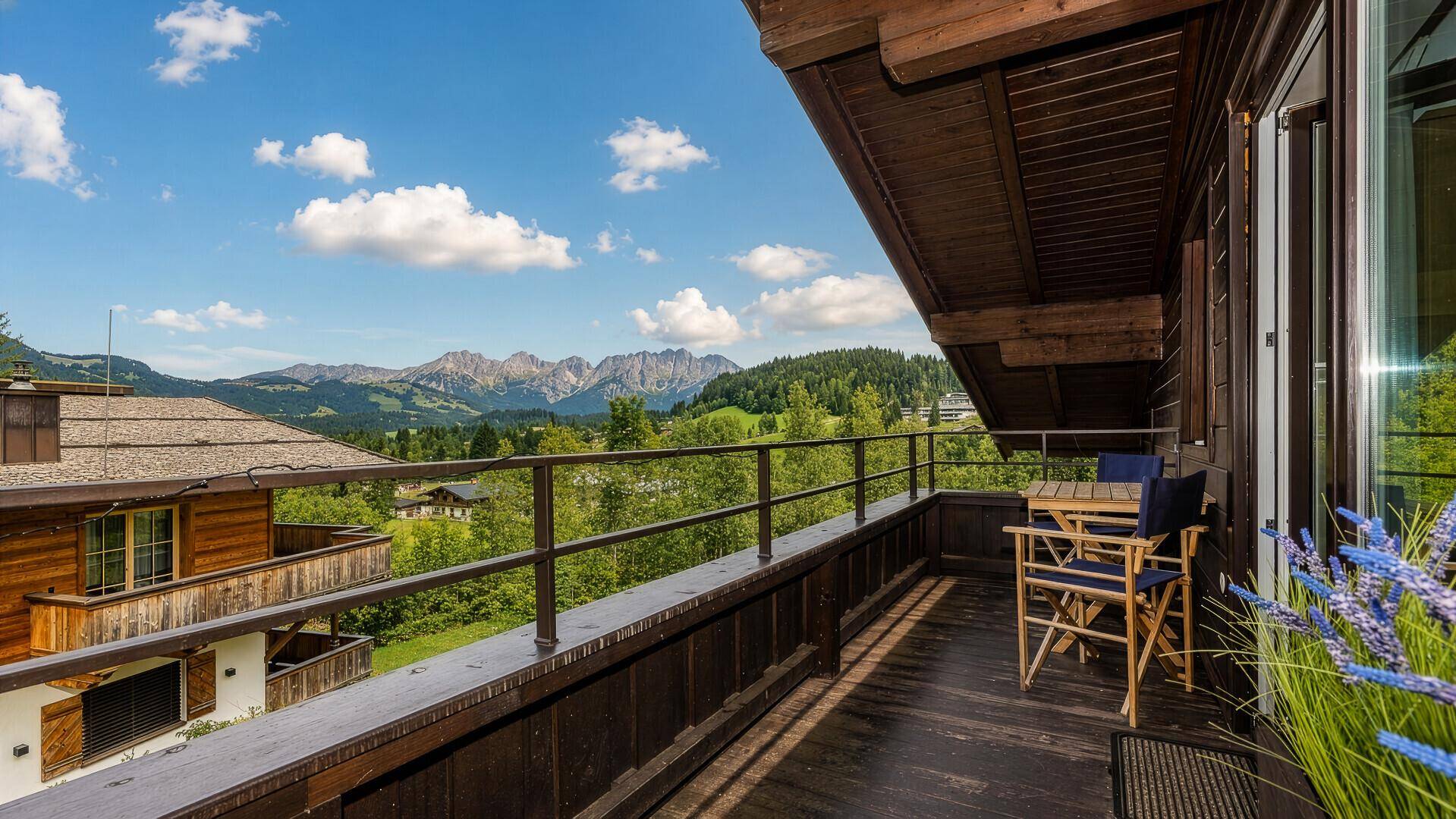 Sonniger Balkon mit Sitzgelegenheiten, Holzboden und weitem Blick auf die umliegende Berglandschaft.