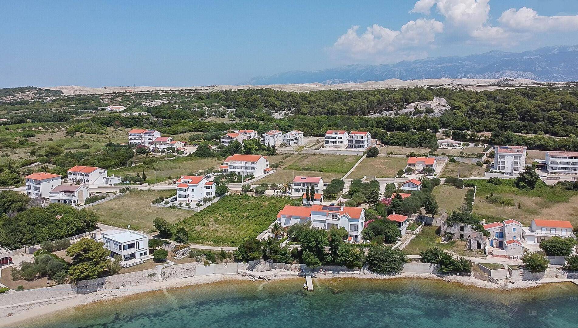 Panoramablick auf die Küstenlandschaft mit Wohngebäuden und dem klaren blauen Meer unter strahlendem Himmel.