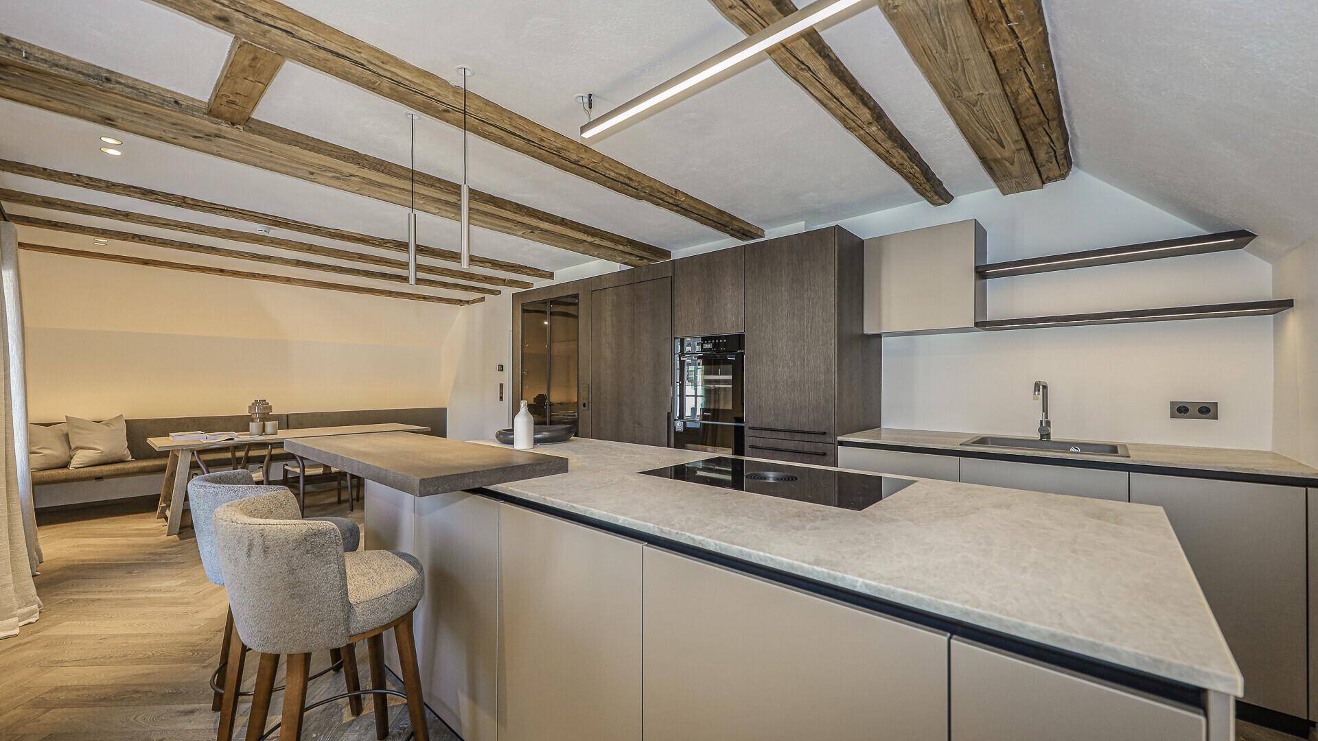 Moderne Küche mit Kochinsel, integrierten Geräten und Holzbalkendecke im alpinen Stil.