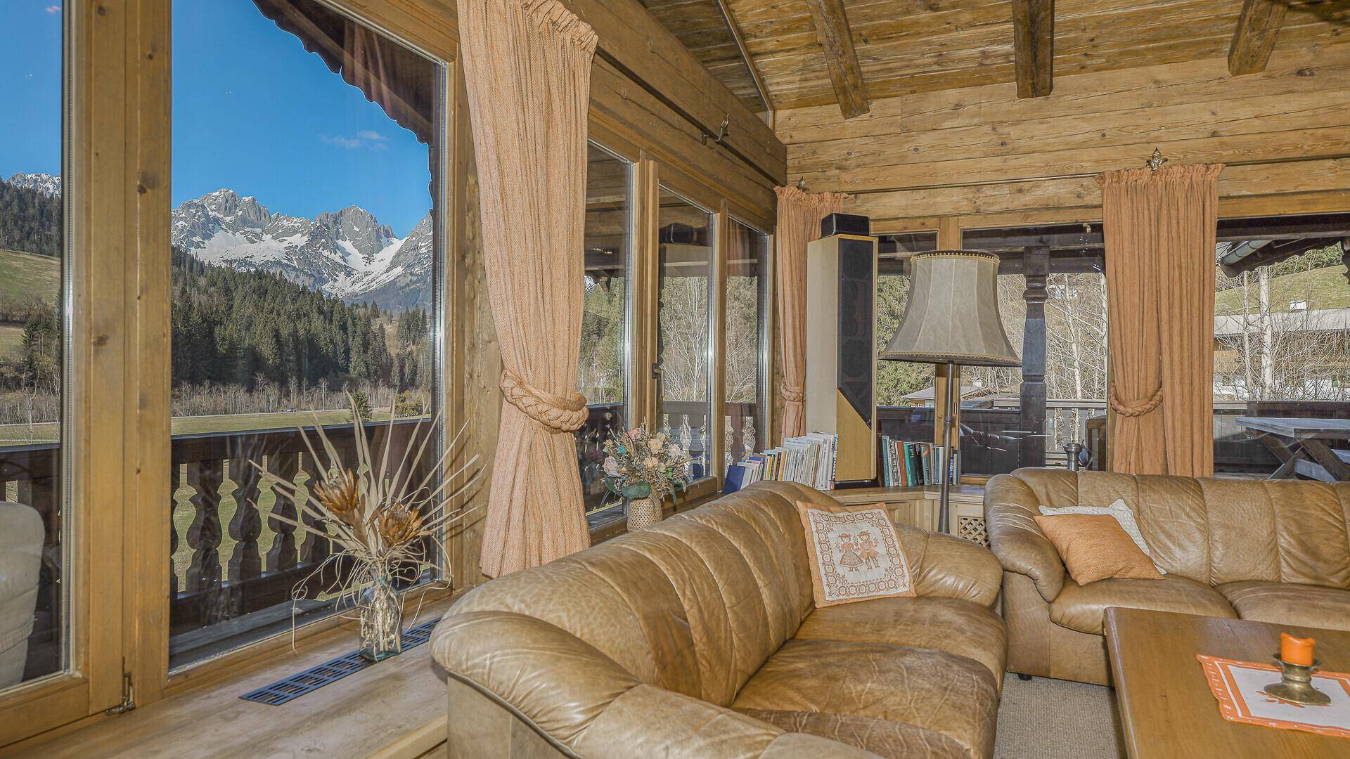 Helles Wohnzimmer mit Ledersofa, Holzbalkendecke und direktem Zugang zum Balkon mit Bergblick.