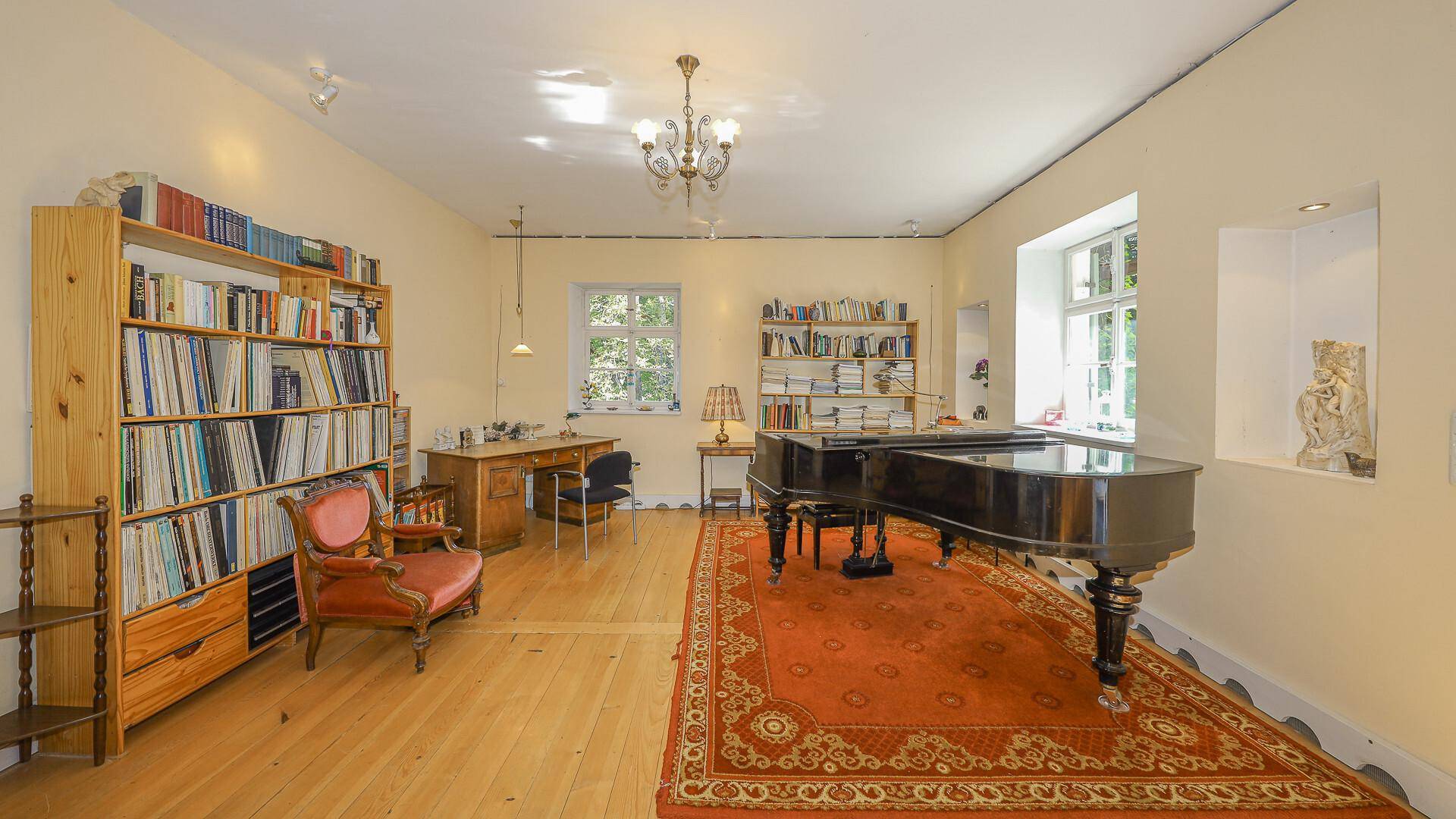 Großer Raum mit Flügel, Bücherregalen und Schreibtisch, ideal als Arbeits- oder Musikzimmer.