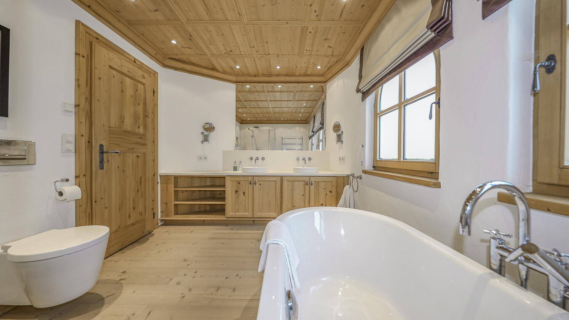 Geräumiges Badezimmer mit Doppelwaschbecken, freistehender Badewanne und Holzbalkendecke.