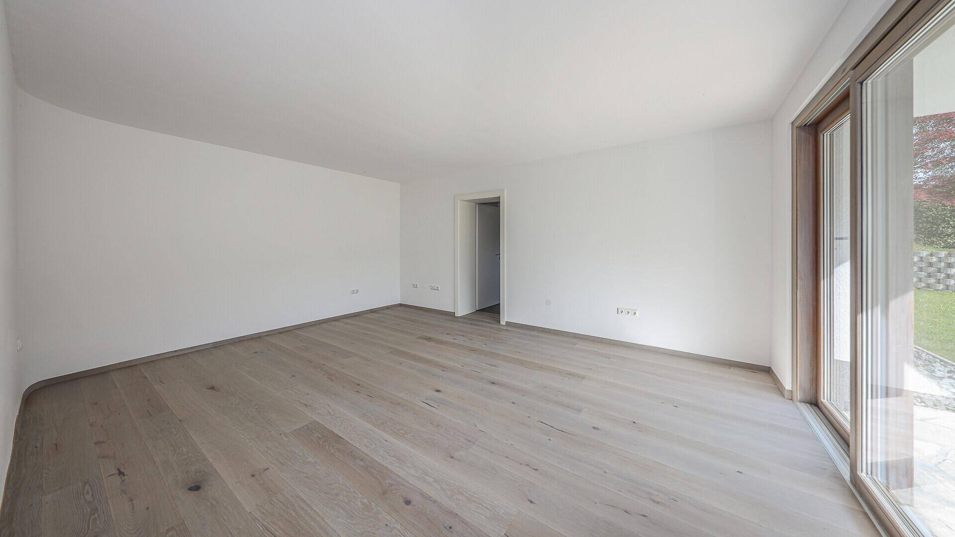 Geräumiges, helles Zimmer mit Holzboden und großer Schiebetür zum Gartenbereich.