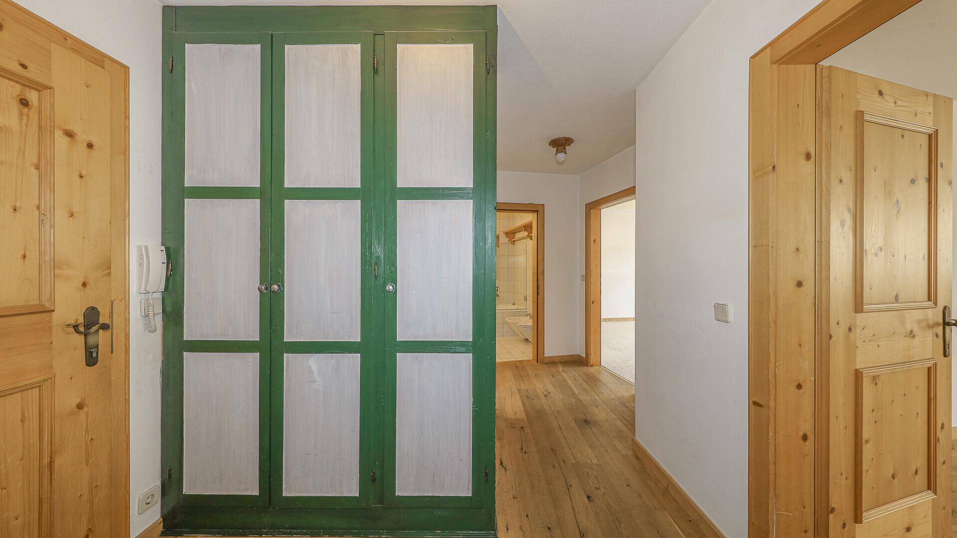 Flur mit Holzboden, Holztüren und einem großen grünen Einbauschrank.