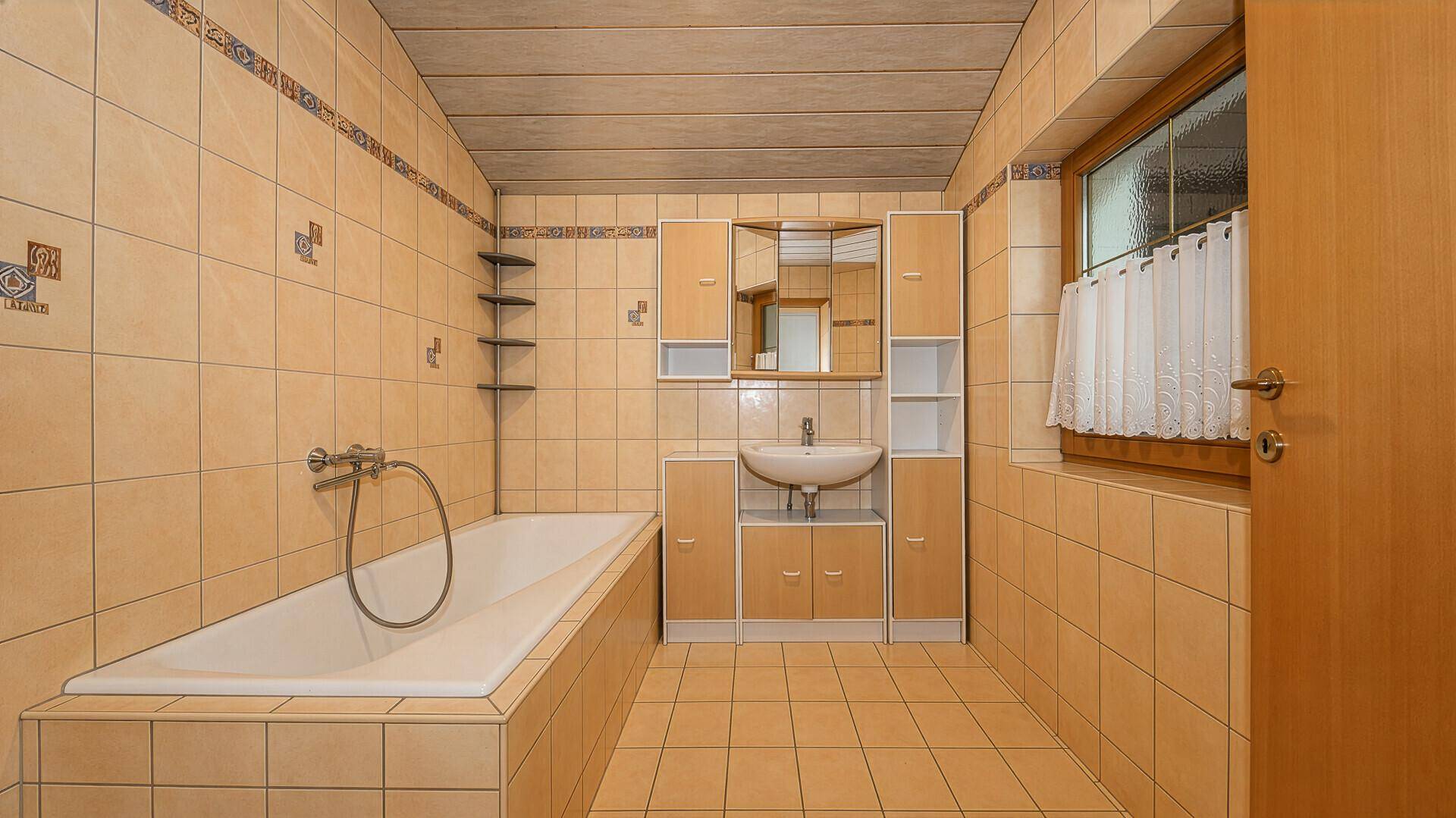 Geräumiges Badezimmer mit Badewanne, Waschbecken und beigefarbenen Fliesen.