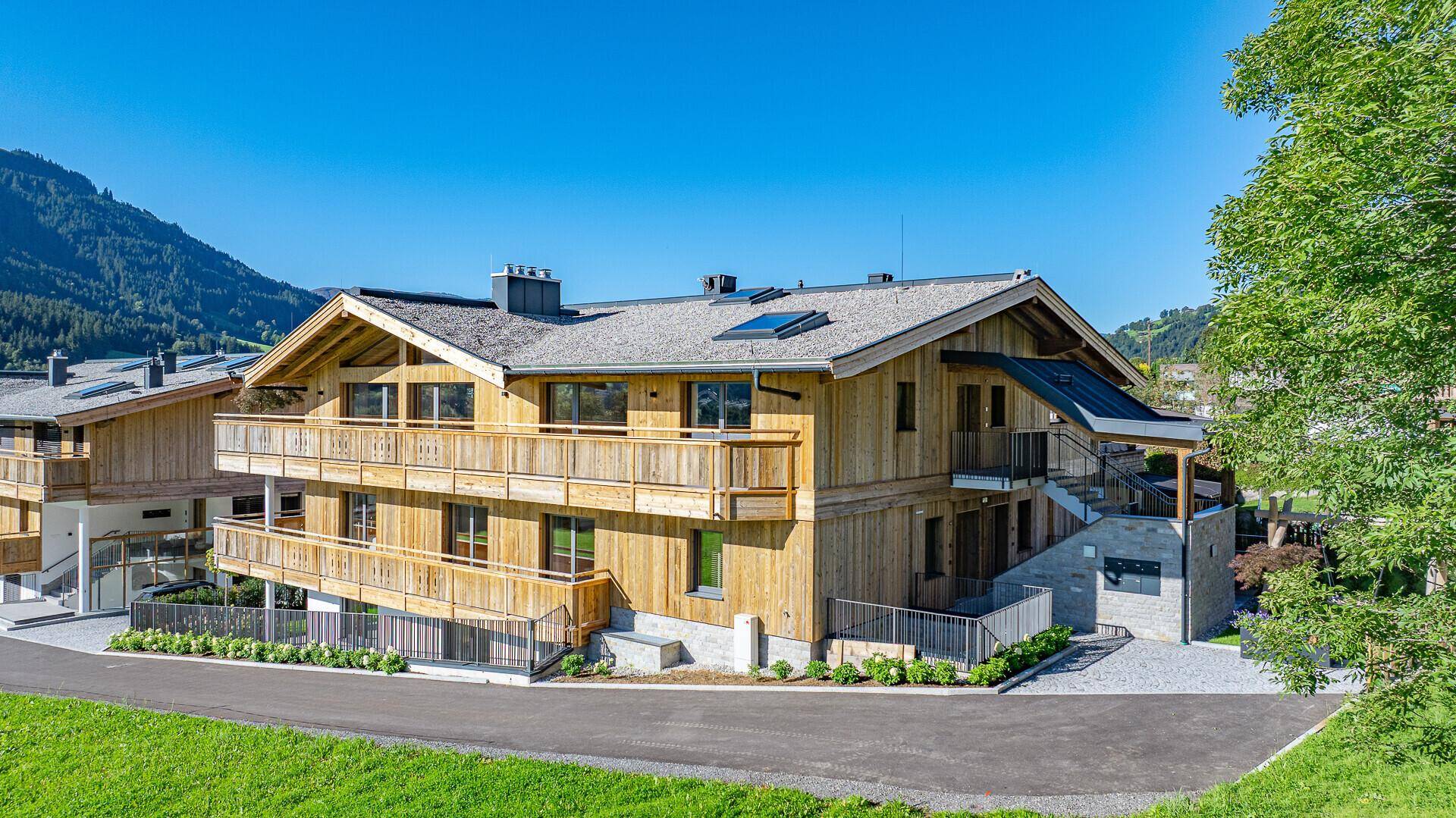 Modernes Mehrfamilienhaus im alpinen Stil mit Holzbalkonen und gepflegter Außenanlage.