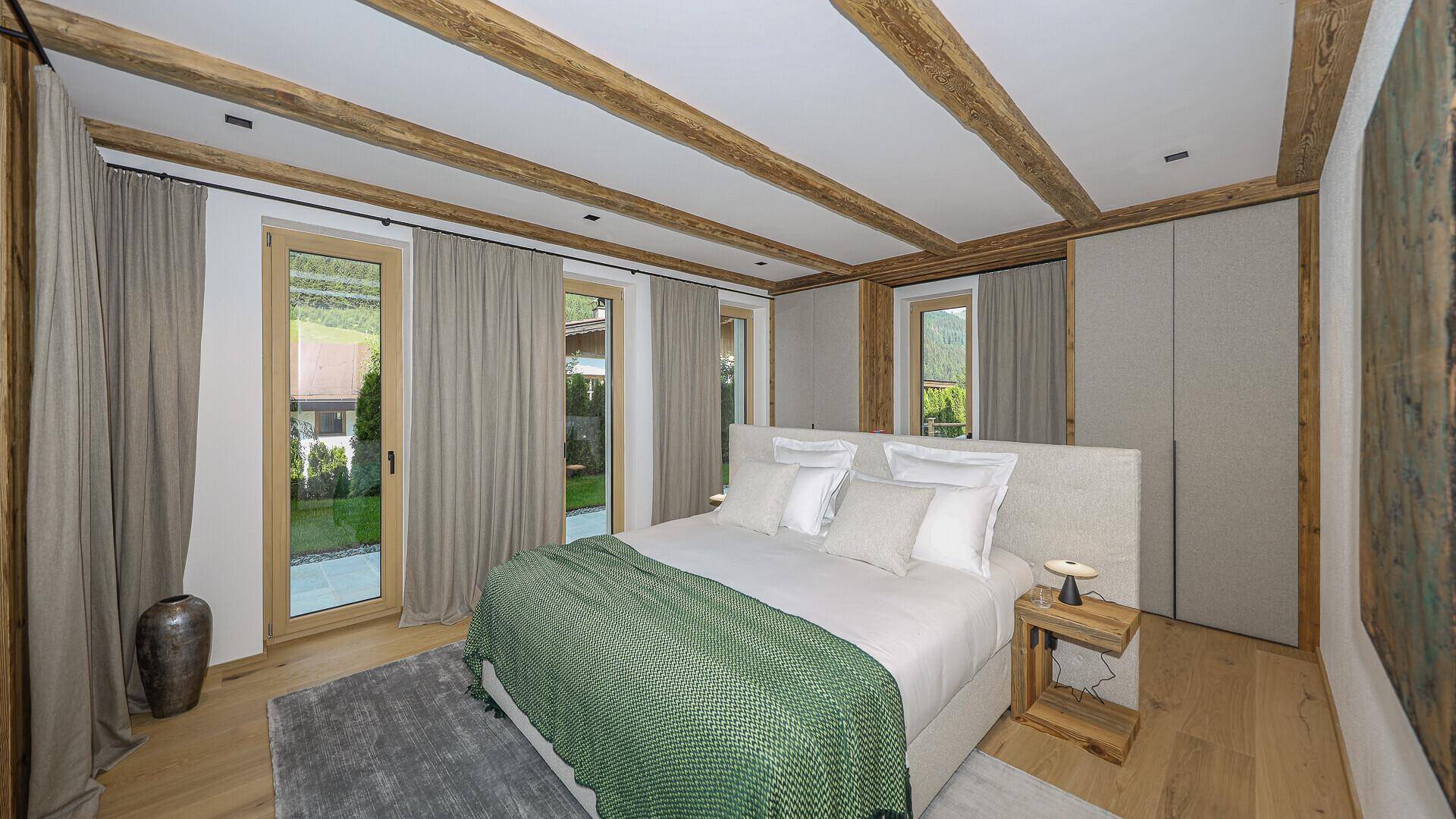 Gemütliches Schlafzimmer mit Holzbalkendecke, Parkettboden und Zugang zum Garten.