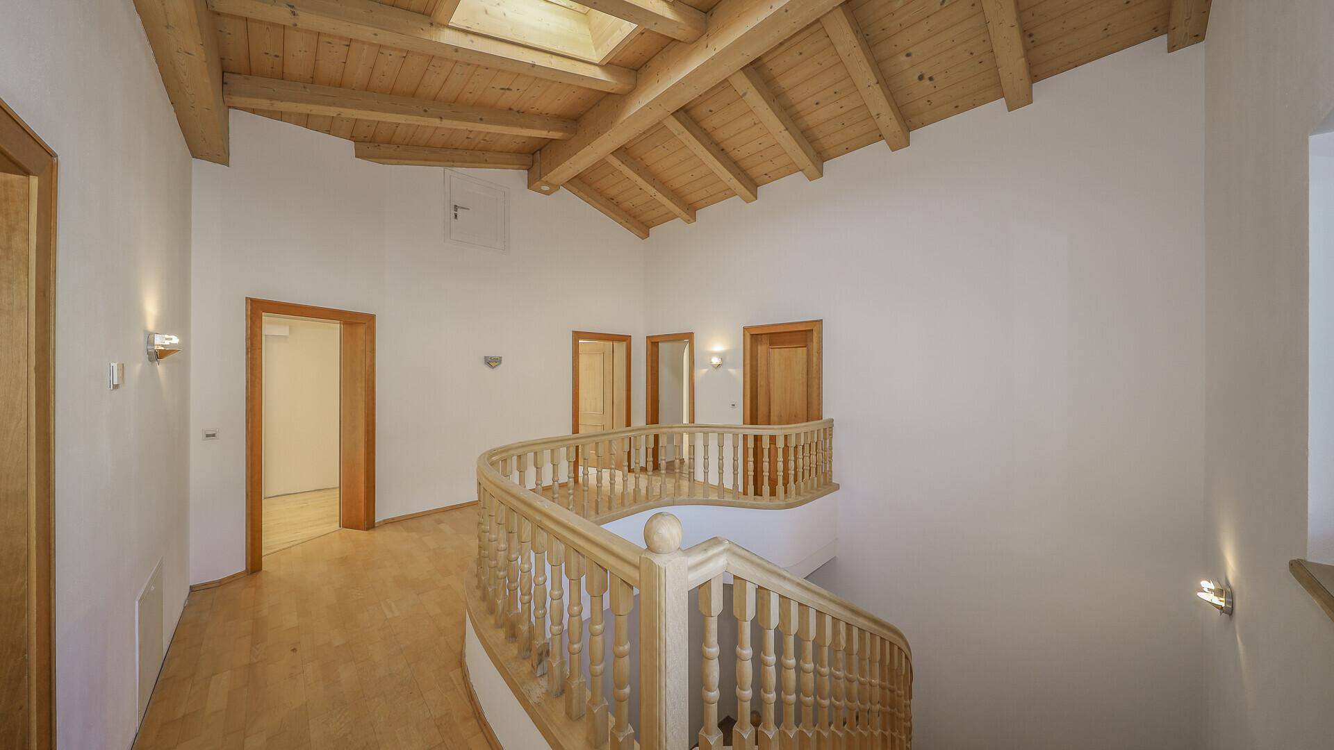 Heller Flur mit Holztreppe, Holzgeländer und sichtbarer Dachkonstruktion mit Oberlicht.