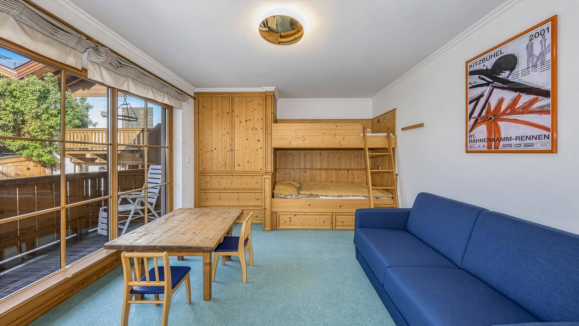 Helles Kinderzimmer mit Etagenbett, kleinem Tisch und großem Fenster mit Balkonzugang.