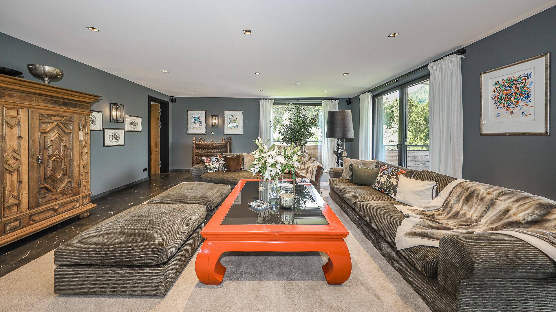 Geräumiges Wohnzimmer mit großem Sofa, auffälligem orangefarbenem Couchtisch und Holzelementen.