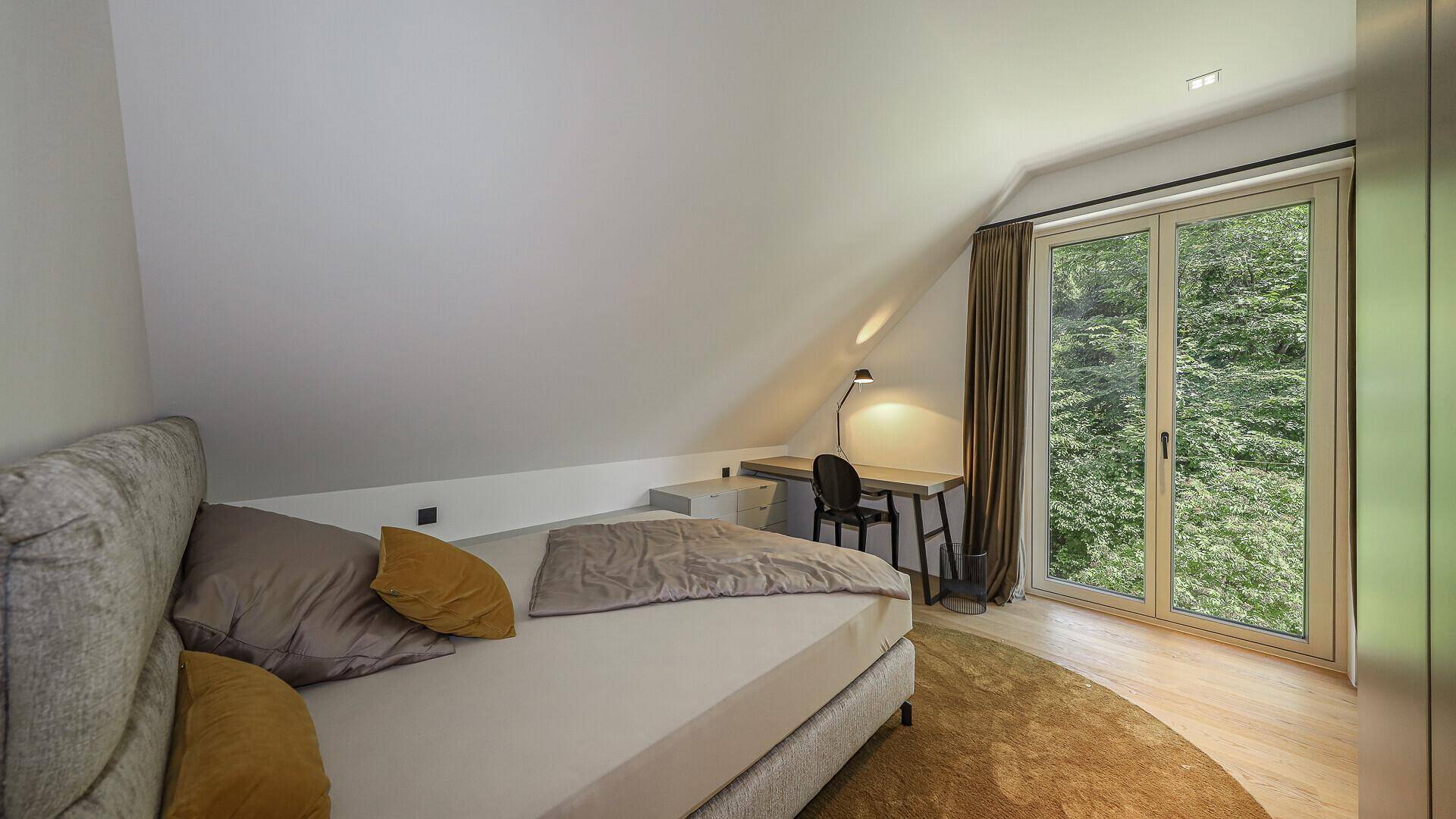 Schlafzimmer im Dachgeschoss mit Zugang zu einem Balkon und Blick ins Grüne.