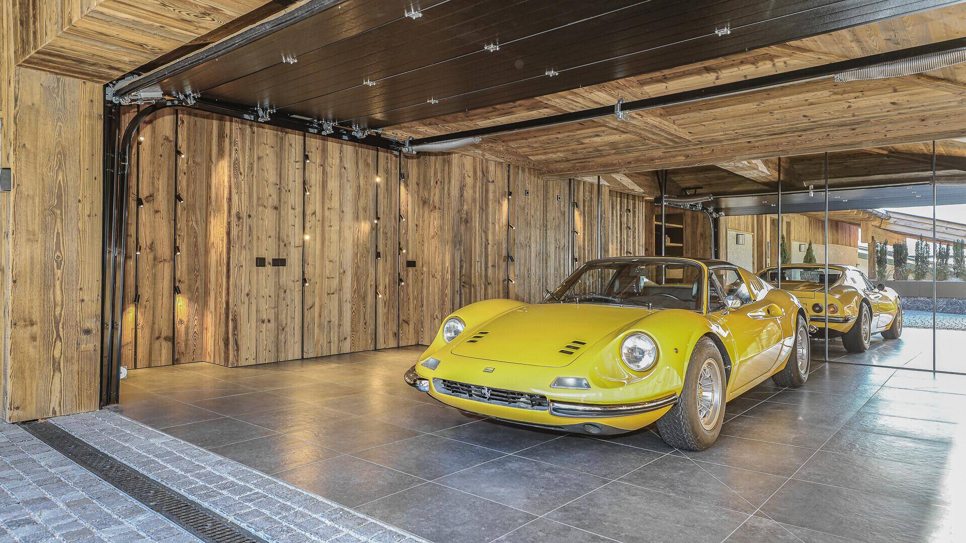 Luxuriöse Garage mit Holzwänden und -decke, in der zwei klassische Sportwagen parken.