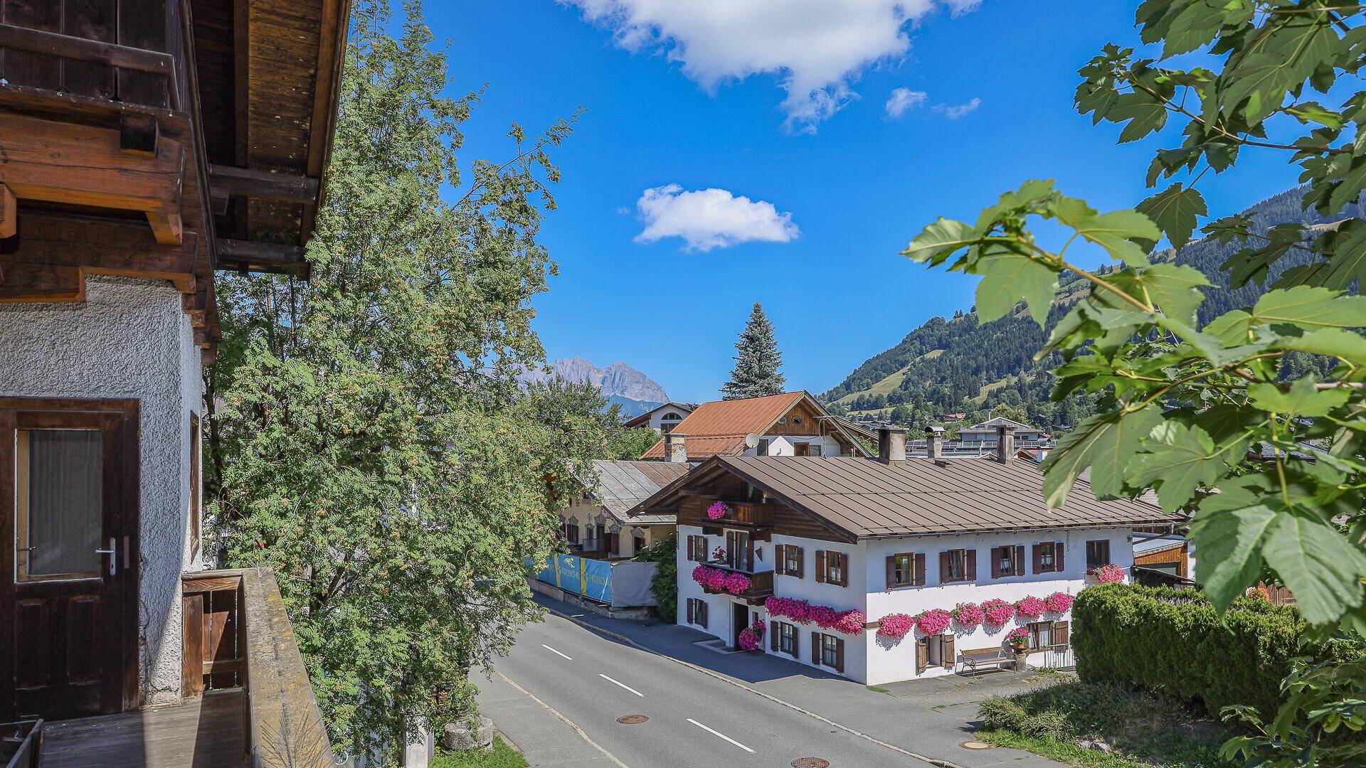 Blick vom Holzbalkon auf die charmante Alpenstadt mit blühenden Blumenkästen und Bergen.