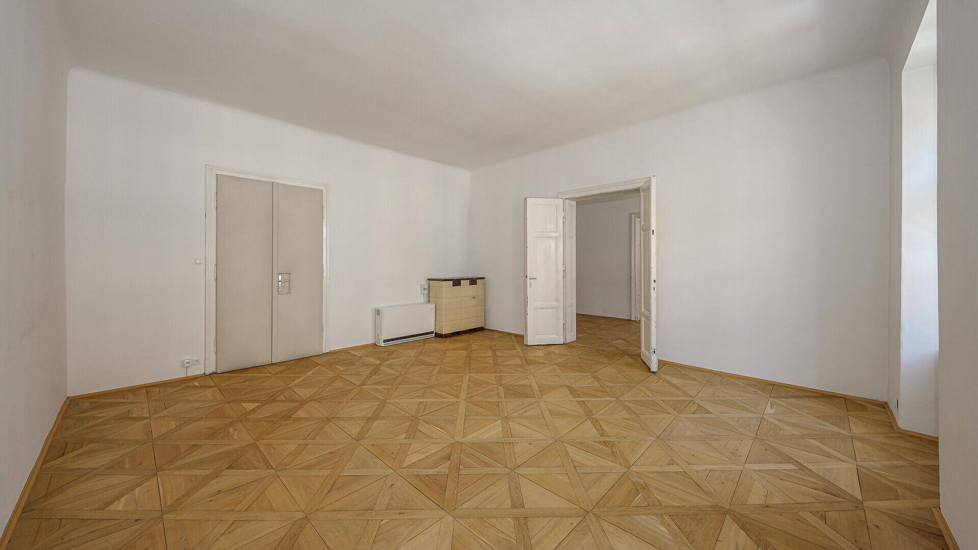 Leeres Zimmer mit Parkettboden, hohen Decken und Doppeltüren zu angrenzenden Räumen.