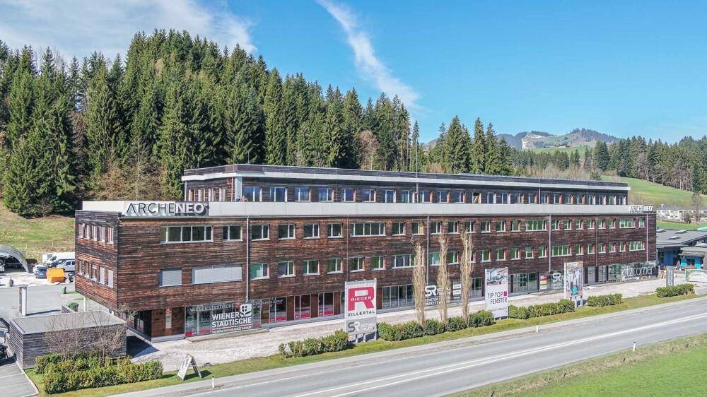 Großes Gebäude mit Holzfassade und vielen Fenstern, umgeben von Bäumen und einer Straße.