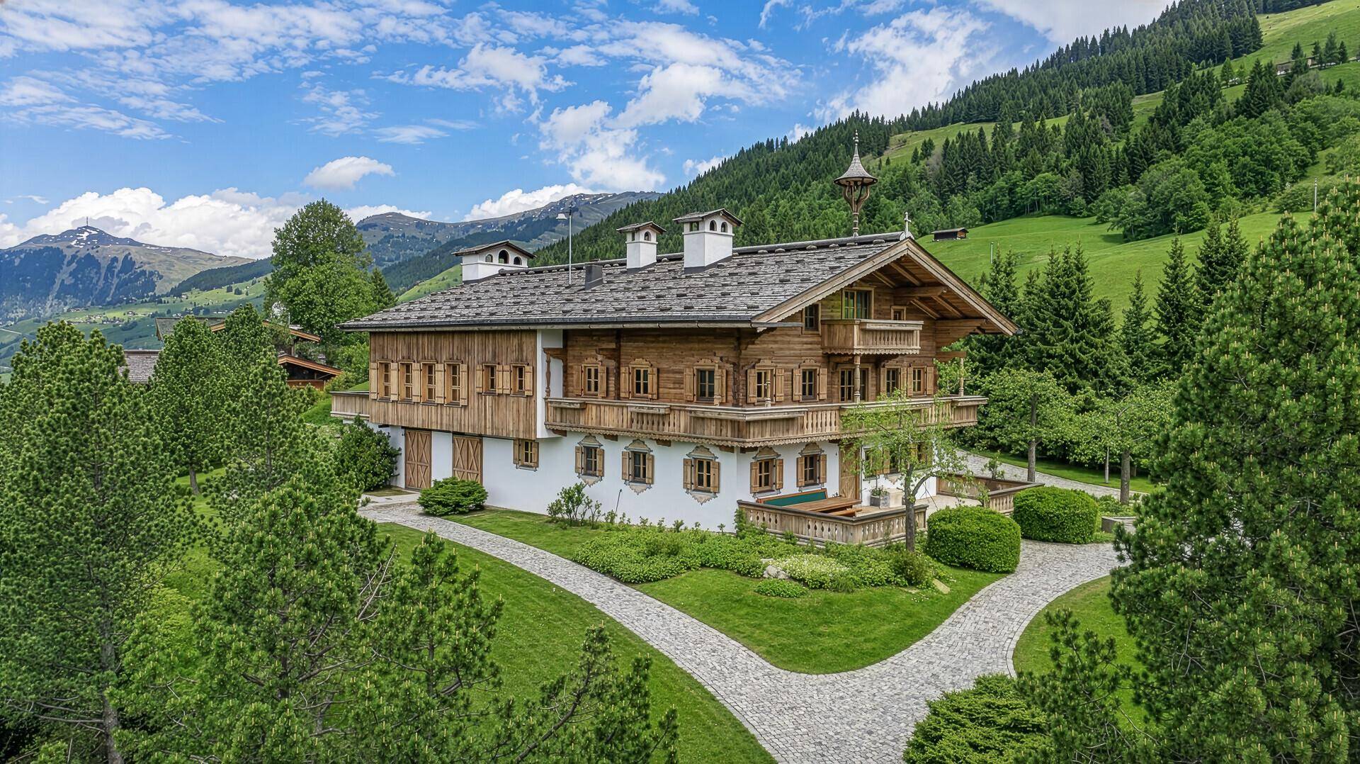 Elegantes Holzchalet mit weißer Fassade und traditionellen Holzbalkonen, eingebettet in eine grüne Landschaft.