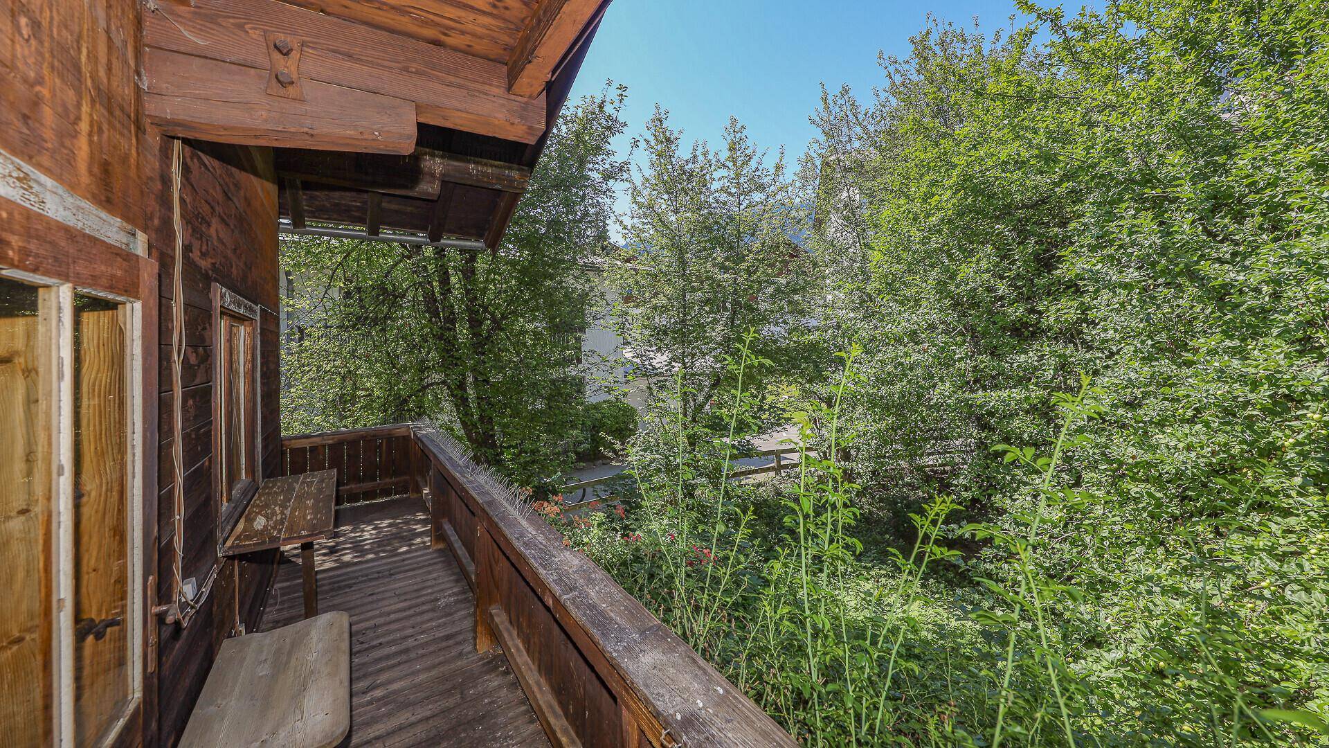 Holzbalkon mit Blick ins Grüne, umgeben von üppigen Bäumen und Sträuchern.