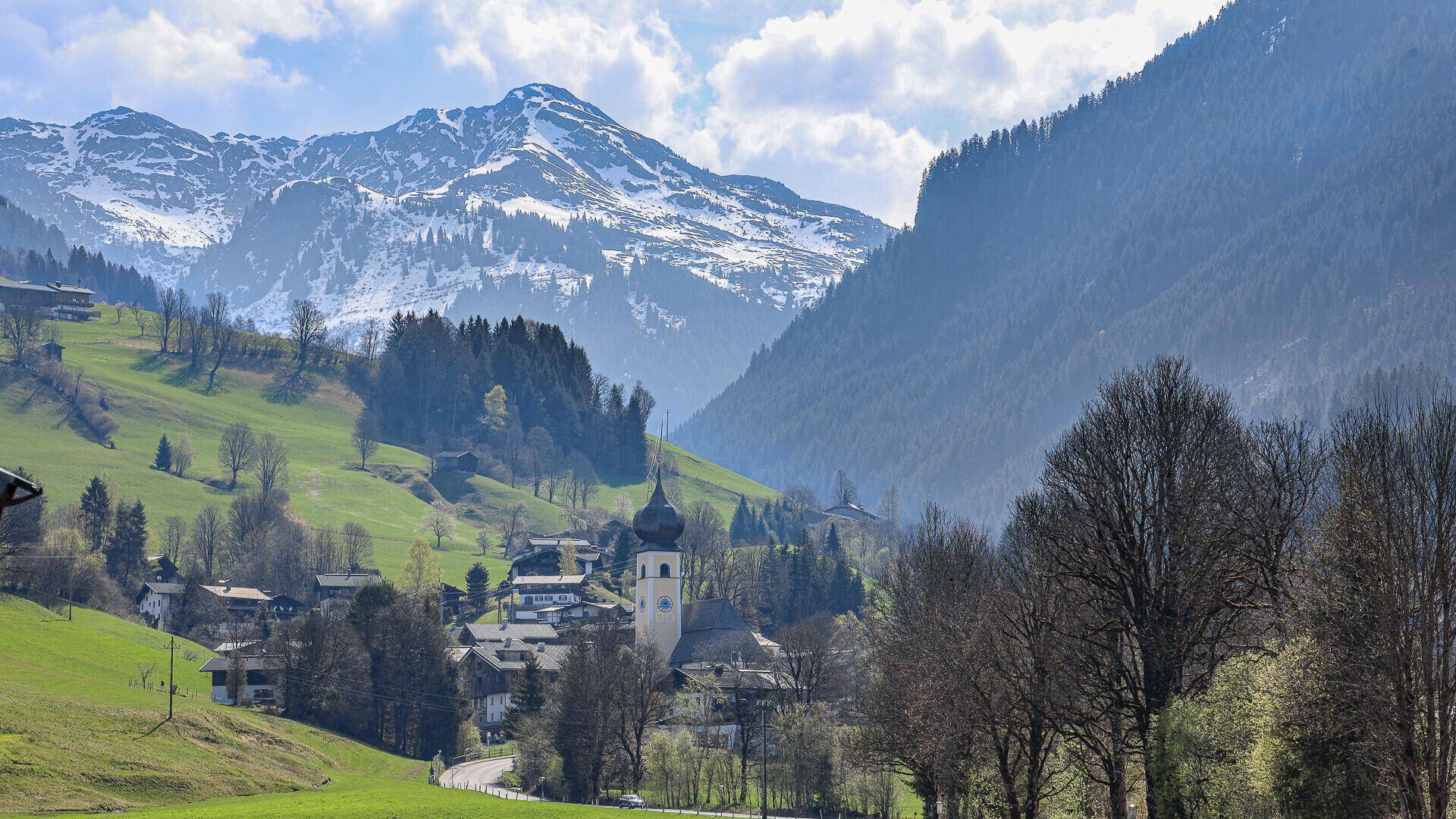 Panoramablick auf ein charmantes Bergdorf mit Kirche, umgeben von majestätischen Alpen und grünen Tälern.