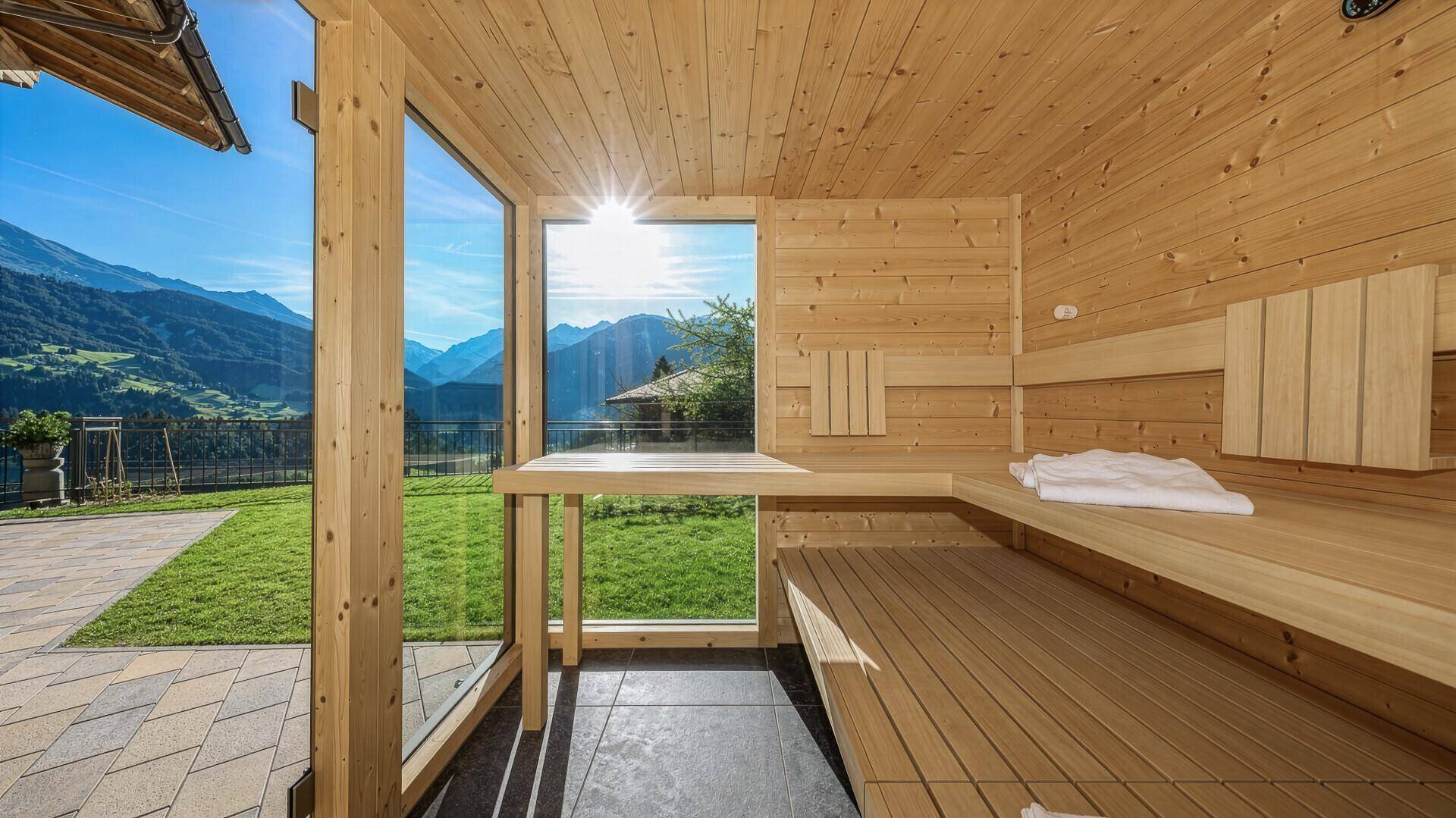 Helle Holzsauna mit Panoramablick auf die Berge und die umliegende grüne Landschaft.