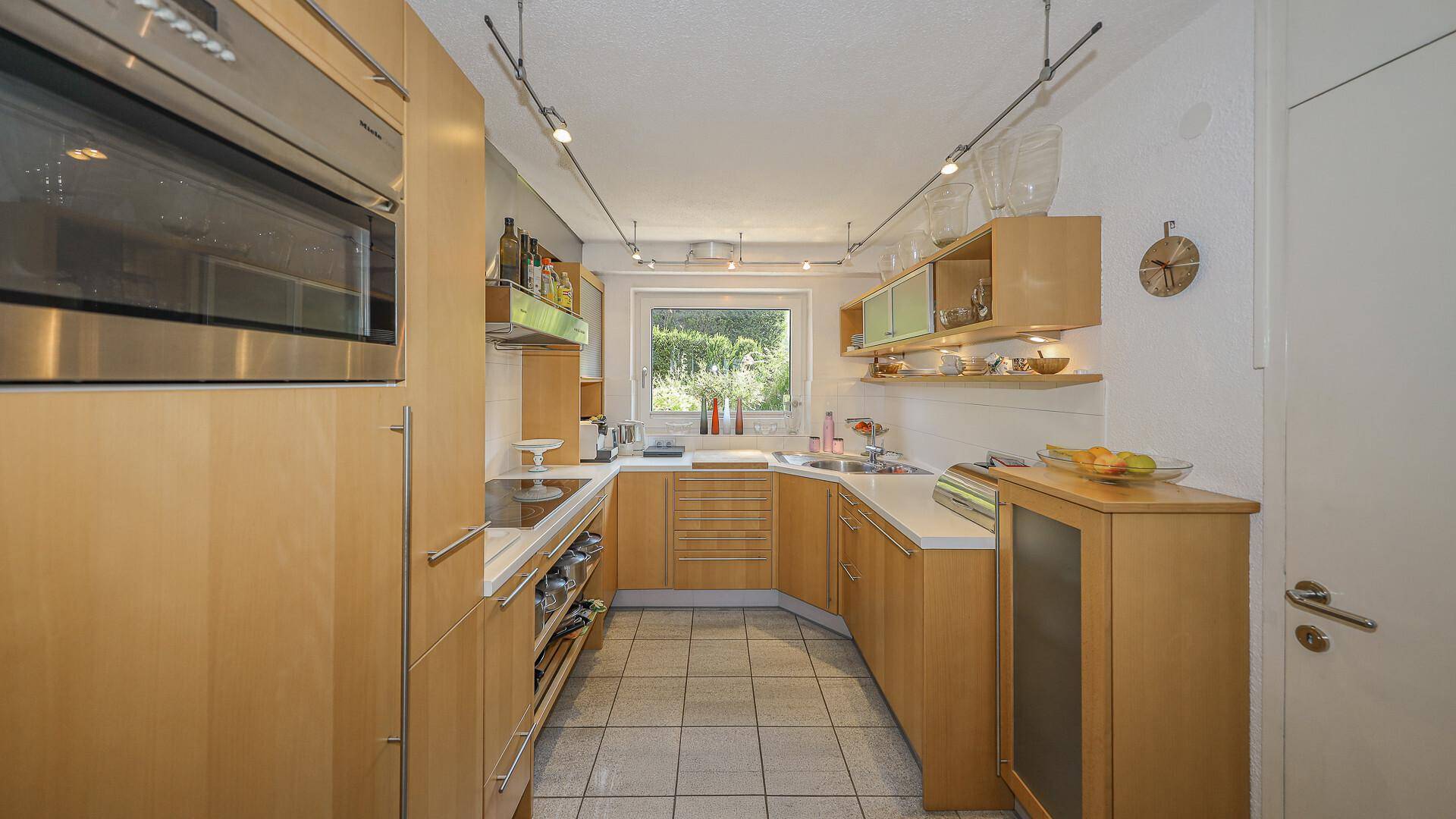 Funktionale Küche mit hellen Holzschränken, Einbaugeräten und Fenster zum Garten.
