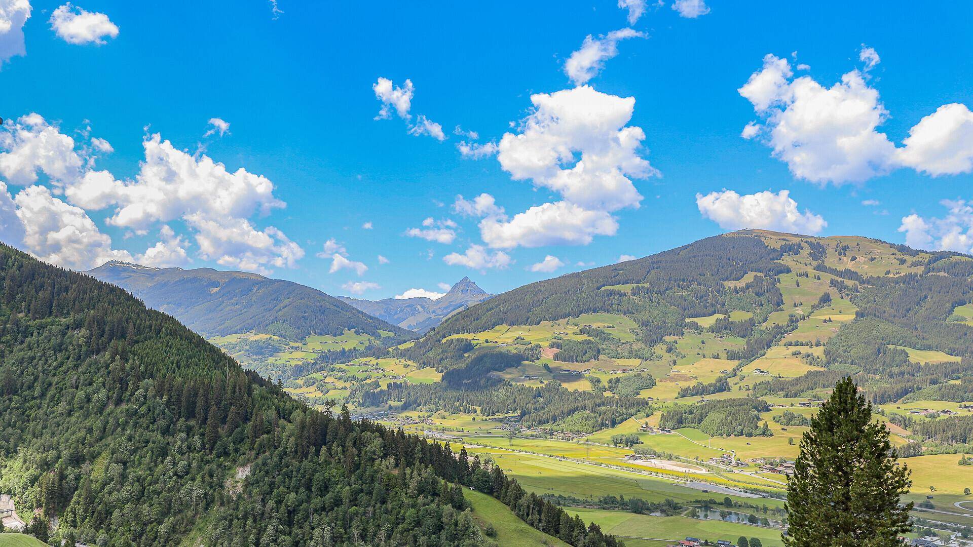 Malerische Berglandschaft mit grünen Tälern und bewaldeten Hängen unter blauem Himmel.