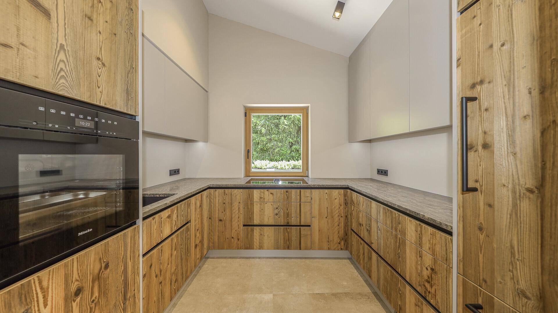 Moderne Holzküche mit Granitarbeitsplatte, Einbaugeräten und Fenster mit Grünblick.