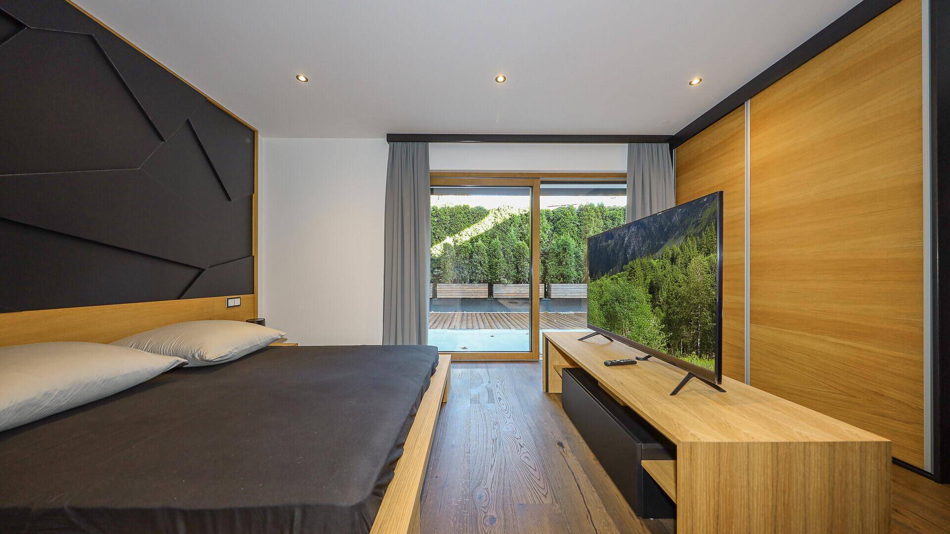 Modernes Schlafzimmer mit Holzboden, Einbauschrank und Zugang zu einer Terrasse mit Bergblick.