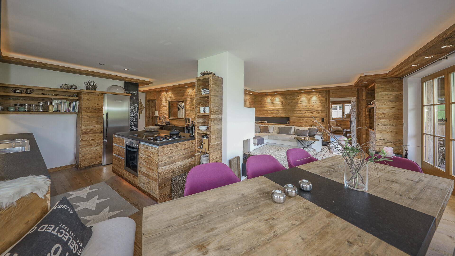 Offener Wohnbereich mit integrierter Küche, Essbereich und Kamin, alles im warmen Holzdesign.