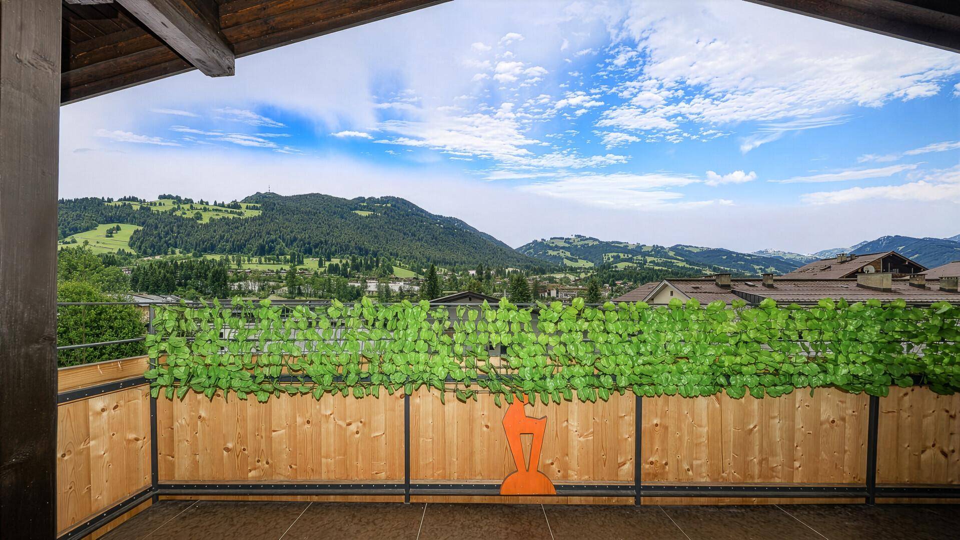 Geräumiger Balkon mit Holzboden und Bergblick, umgeben von grünen Pflanzen.