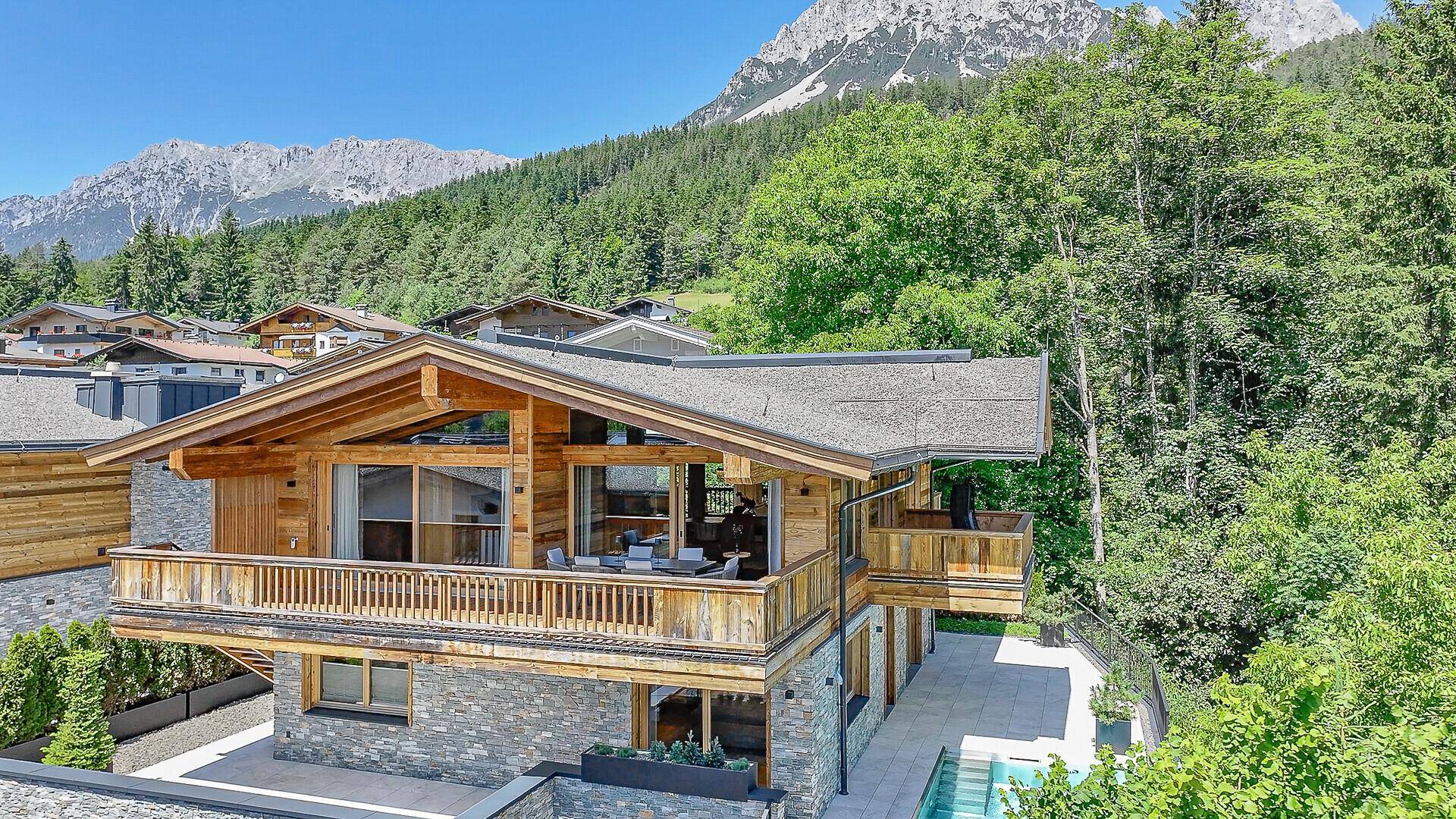 Panoramablick auf das luxuriöse Chalet mit Holzbalkonen und Bergblick in sonniger Lage.