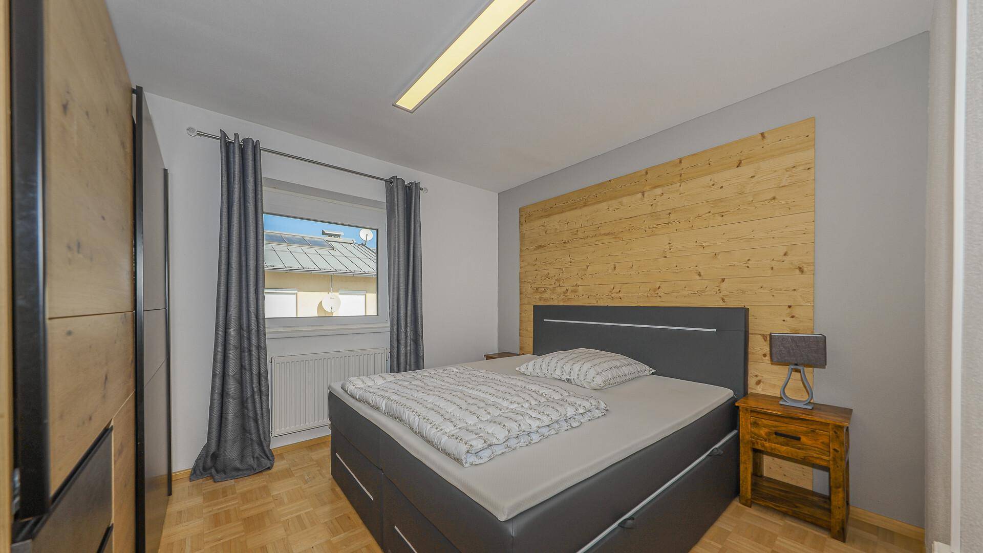 Modern eingerichtetes Schlafzimmer mit Holzwandakzent, Doppelbett und Parkettboden.