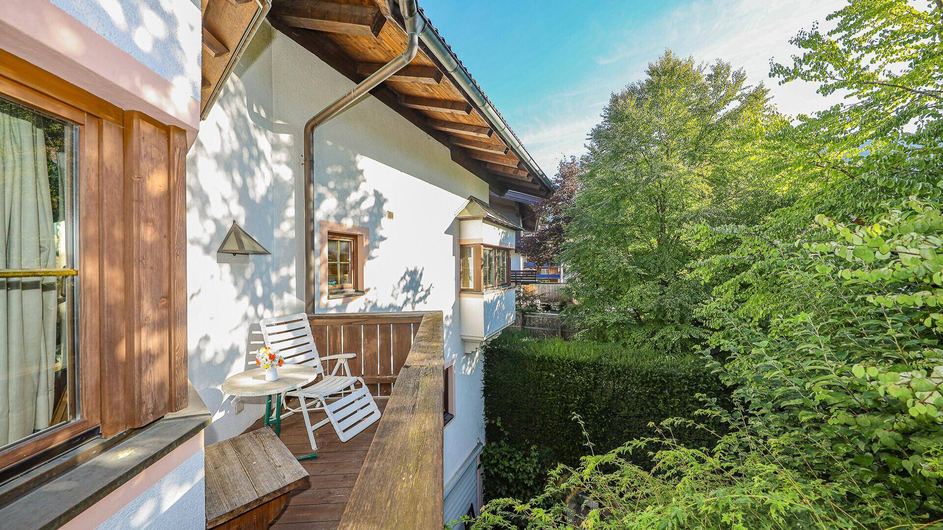 Sonniger Holzbalkon mit Sitzgelegenheiten und Blick auf die grüne Umgebung.