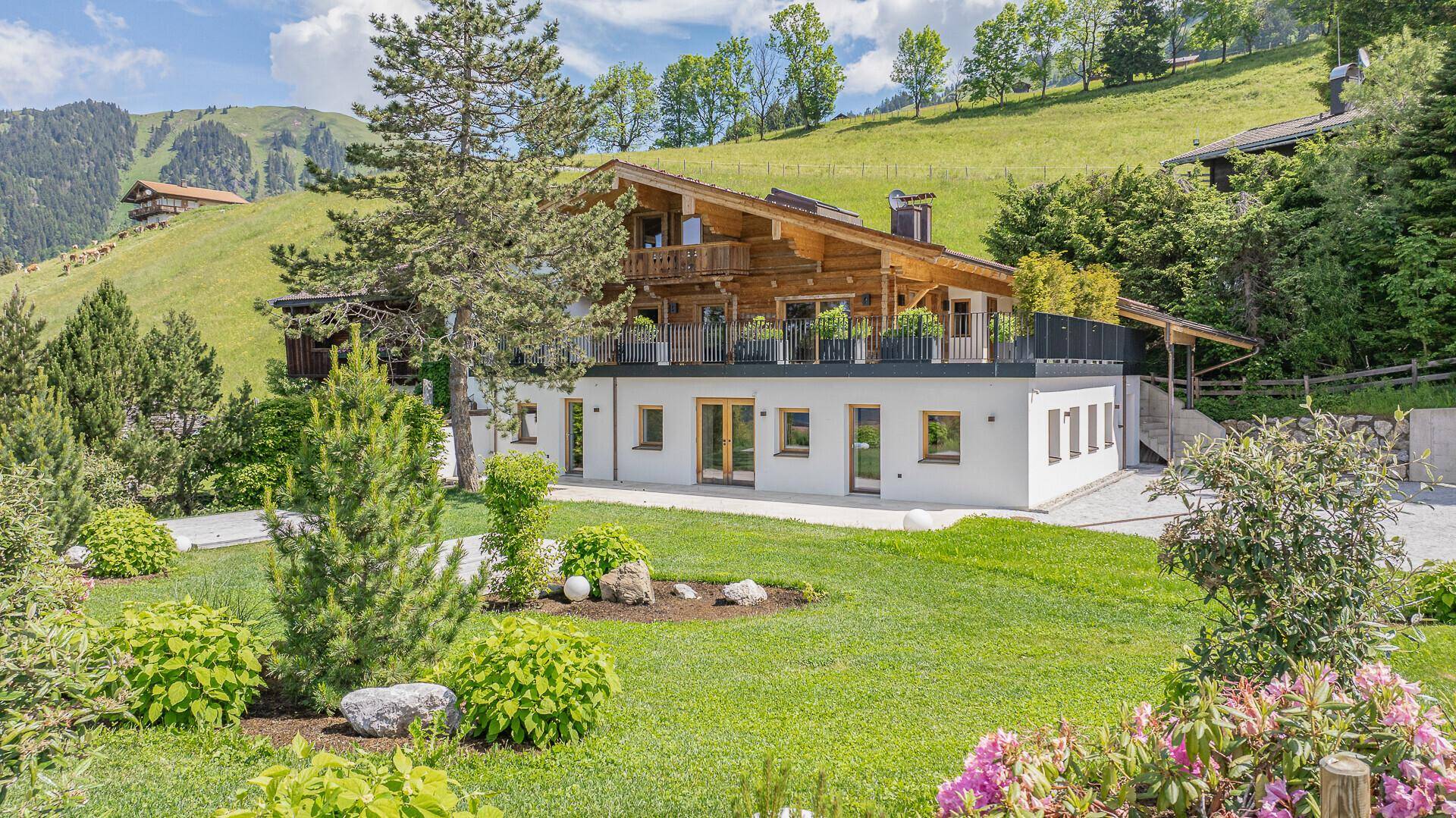 Elegantes Chalet mit Holzfassade und großzügiger Terrasse, umgeben von grüner Natur.
