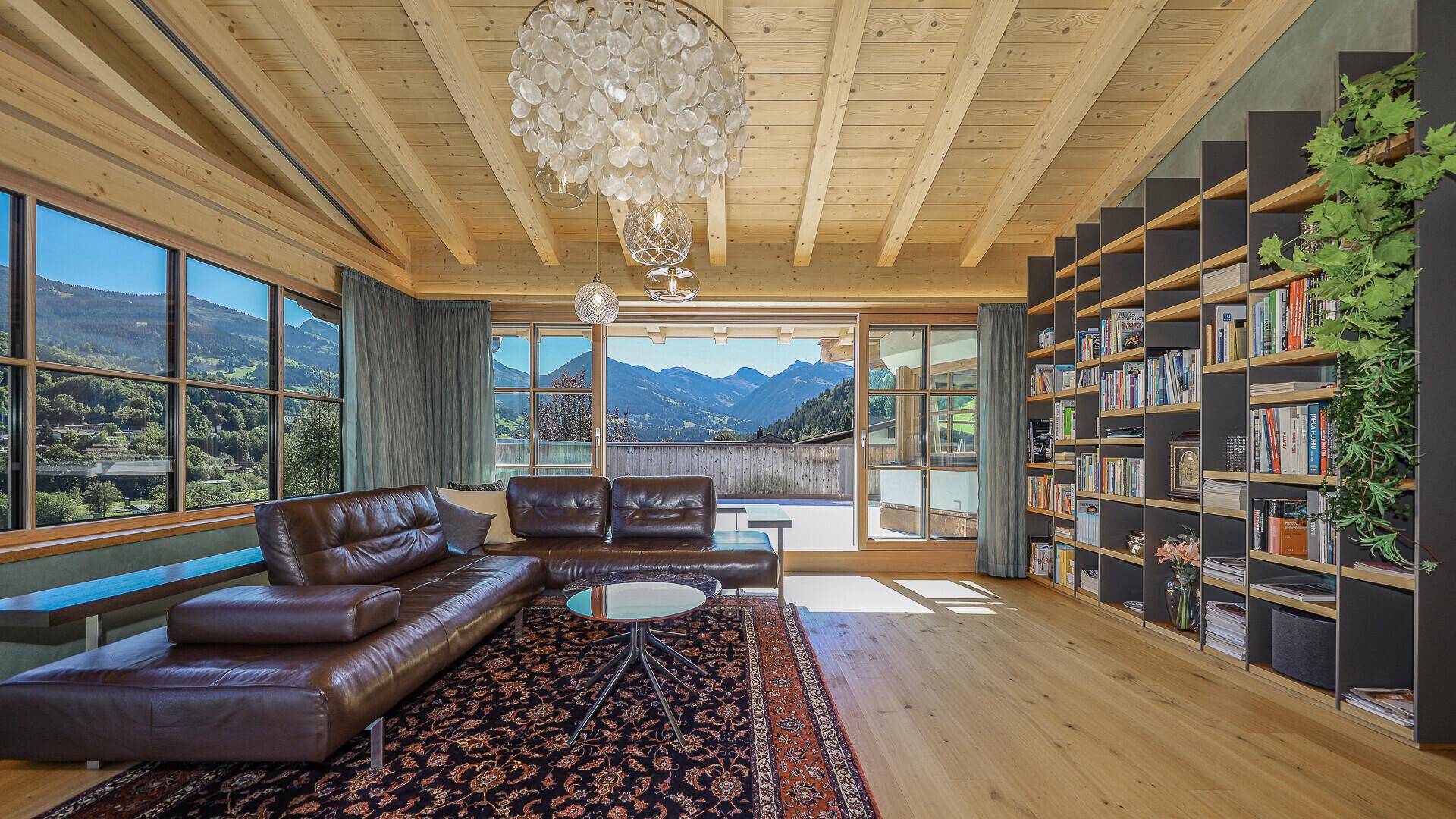 Elegantes Wohnzimmer mit Holzbalkendecke, Ledersofa und großen Fenstern mit Bergblick.
