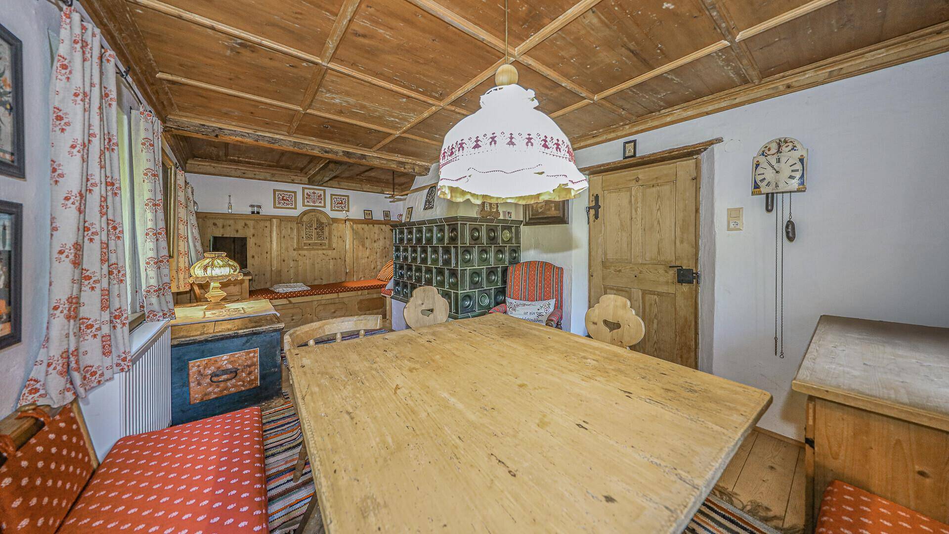 Rustikaler Essbereich mit traditionellem Kachelofen, Holztisch und Holzbalkendecke im Originalzustand.