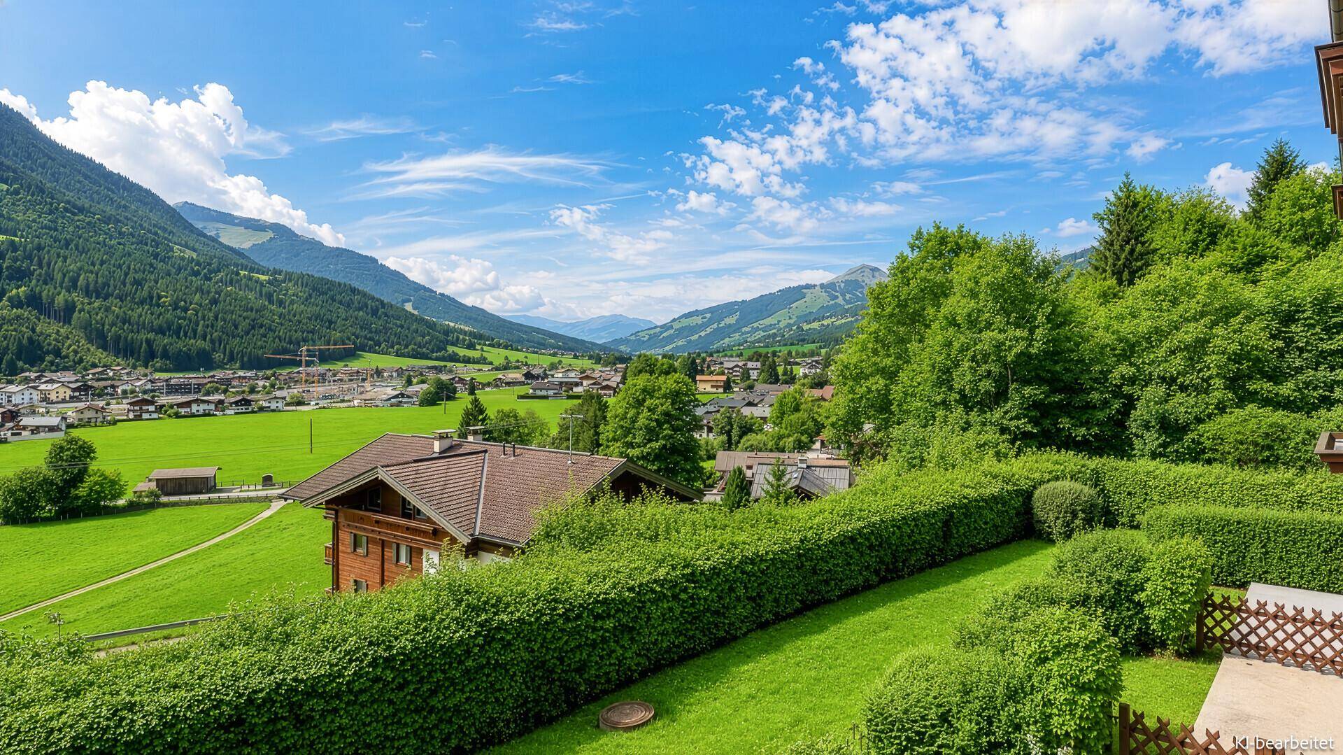 Malerischer Blick über ein grünes Tal mit traditionellen Häusern und bewaldeten Bergen.