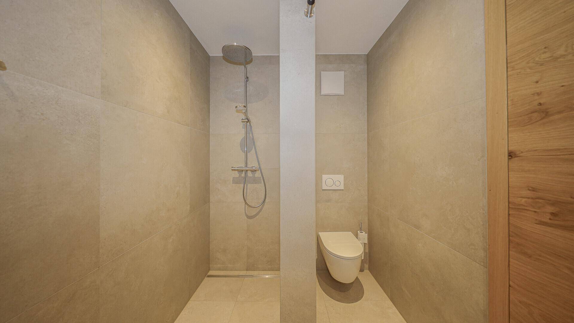 Modernes Badezimmer mit ebenerdiger Dusche und wandhängendem WC in neutralen Farbtönen.