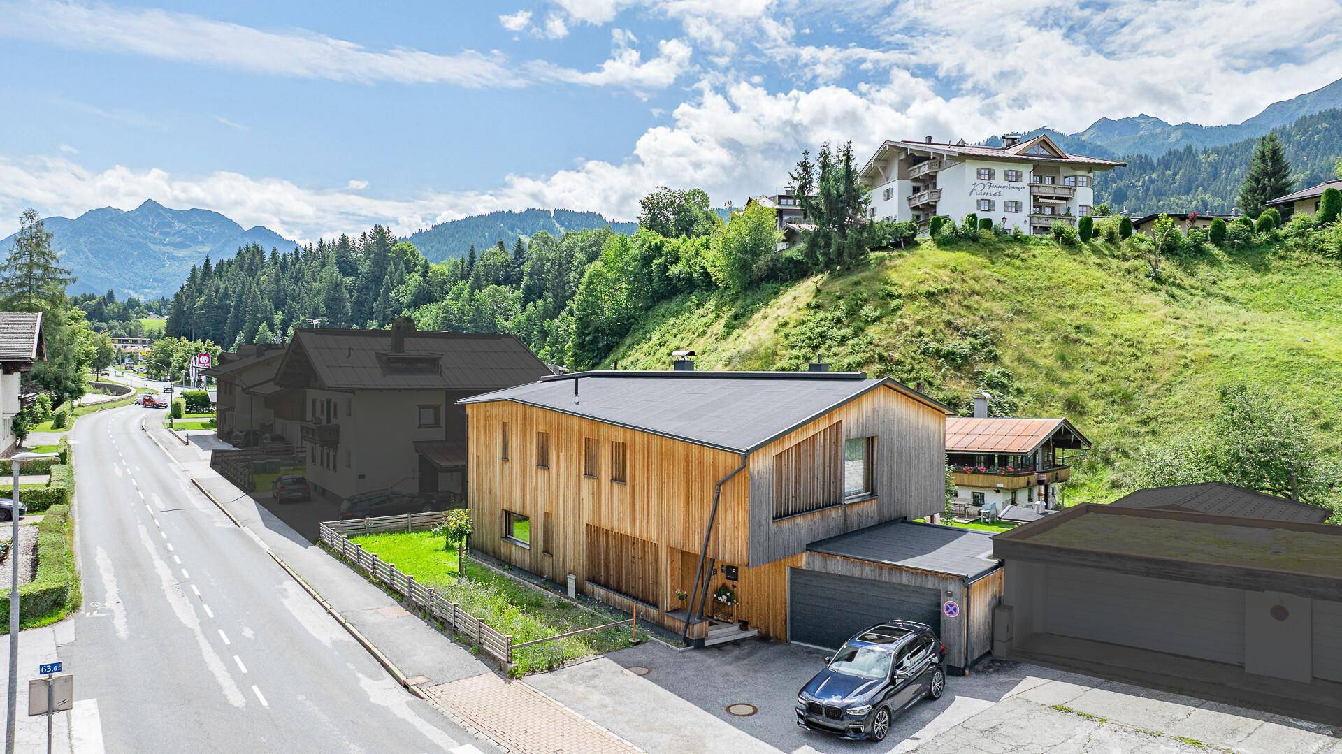 Ansicht des modernen Holzhauses von der Straße mit Garage und umliegender Berglandschaft.